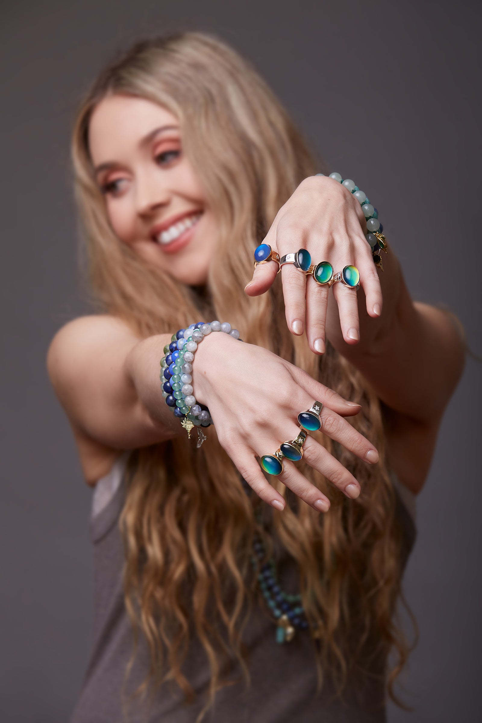 Woman wearing multiple bracelets and silver mood rings on a grey background