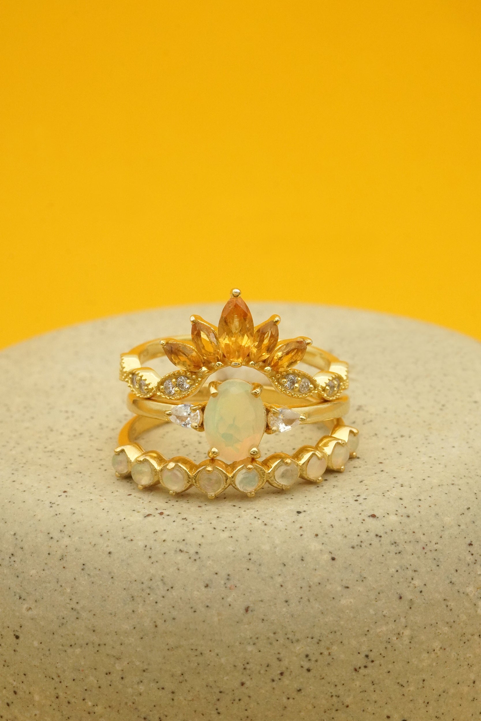 Gold stacking rings with opal and citrine stones on a textured surface with yellow background