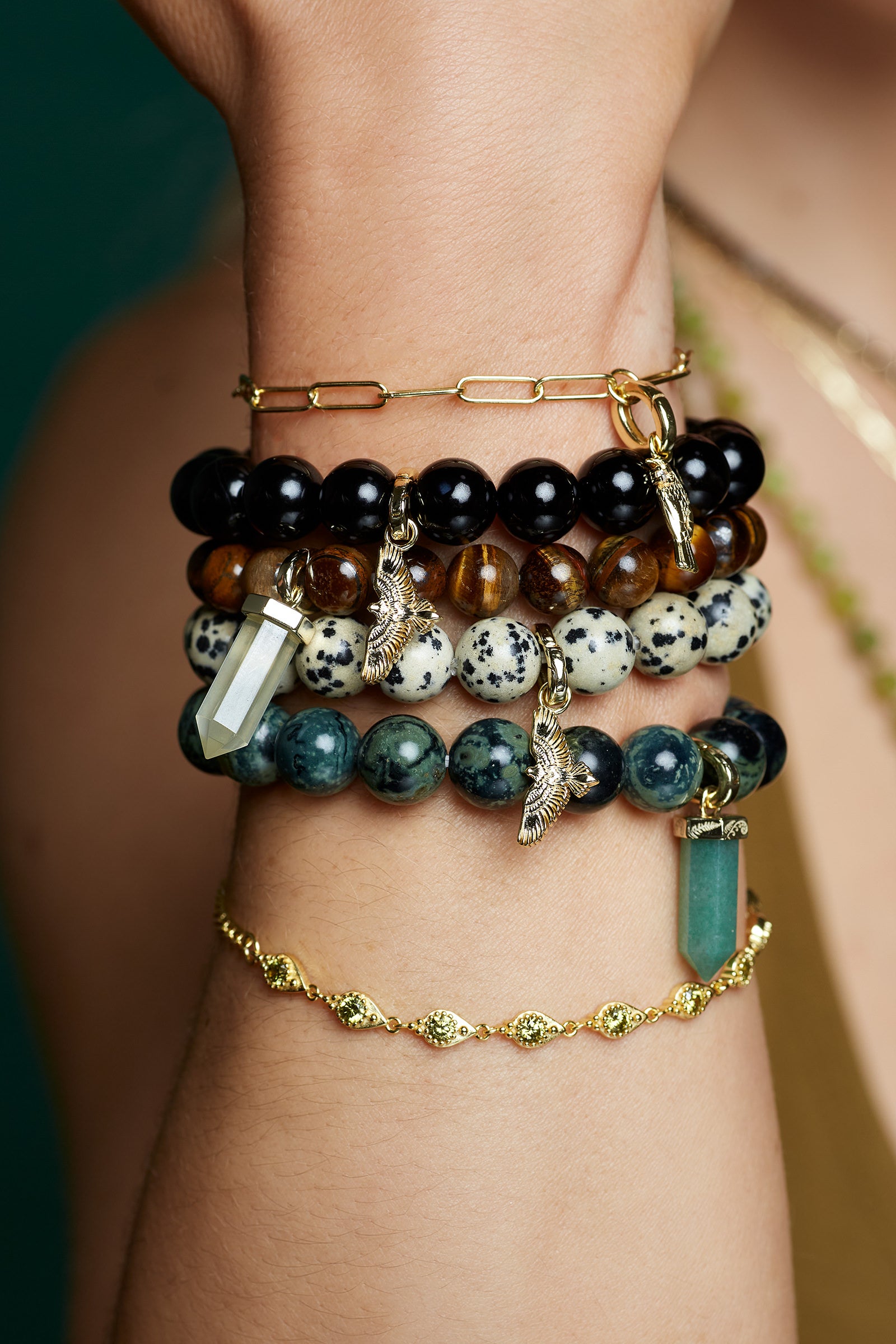 Stack of beaded bird and crystal nature inspired bracelets on a wrist with a blurred background