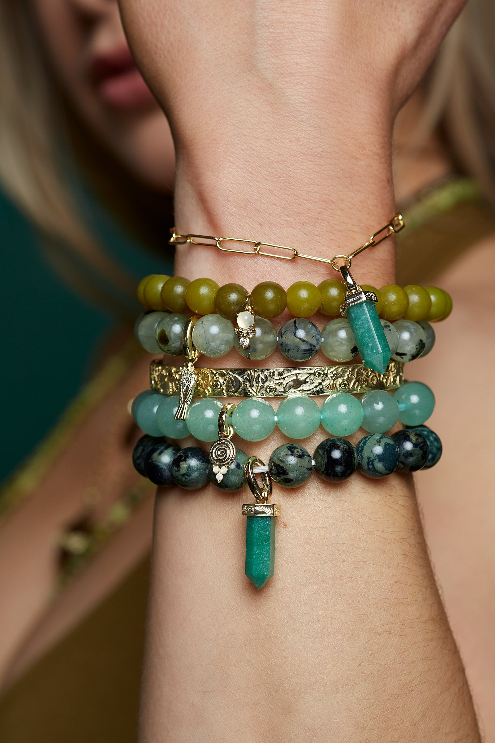 Stack of green earthy natural gemstone  beaded bracelets on a wrist with a blurred background