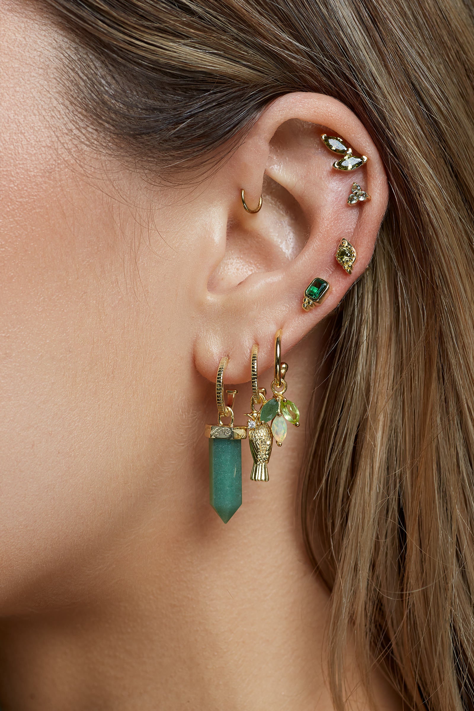 Close-up of an ear with multiple gold and green earrings stacked