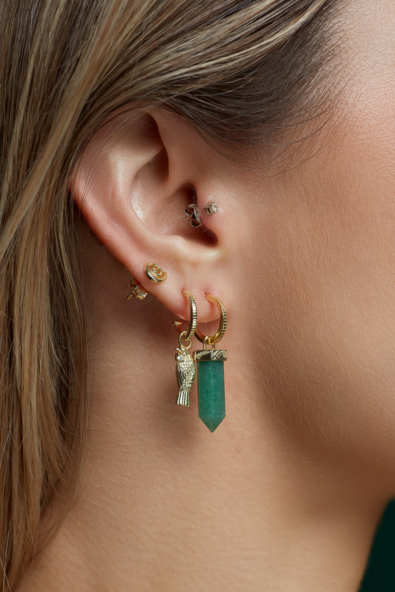 Close-up of an ear with gold hoop earrings featuring green aventurine gemstones.