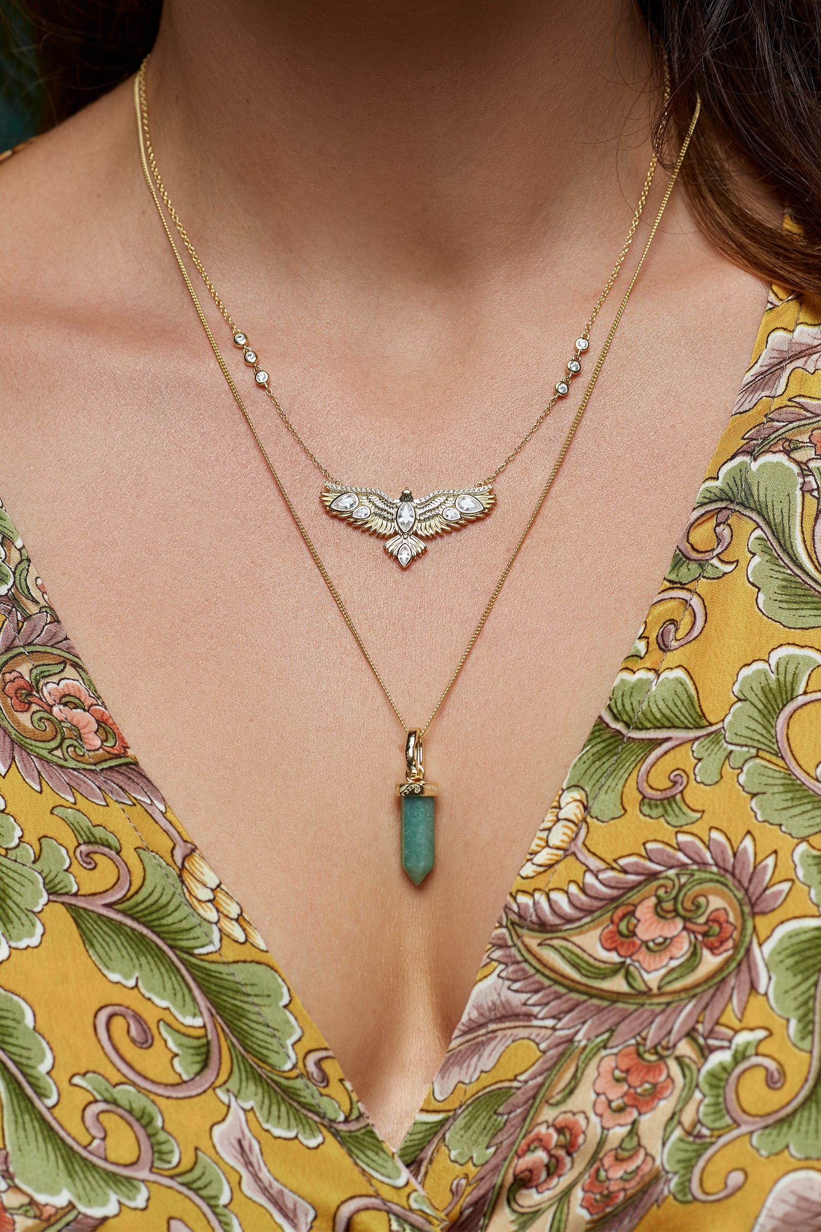 Close-up of a woman wearing two necklaces, a hawk and green crystal with a floral dress.