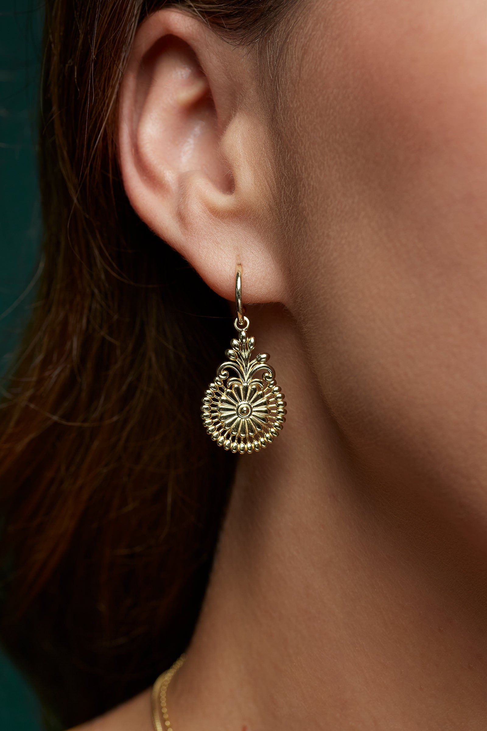 Close-up of a gold floral statement earring worn by a woman with a blurred background