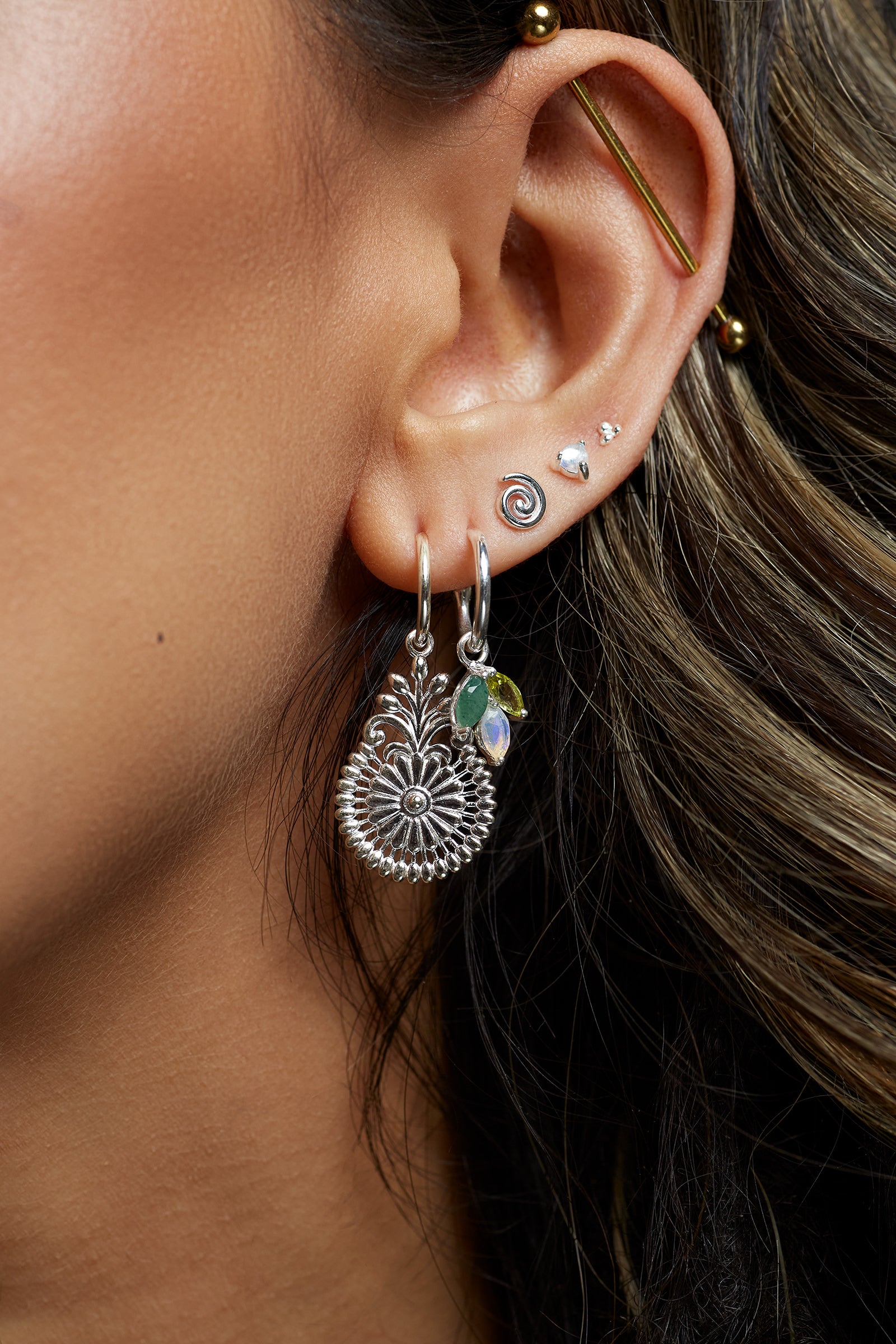 Close-up of an ear with large silver floral statement earrings and other smaller silver earrings