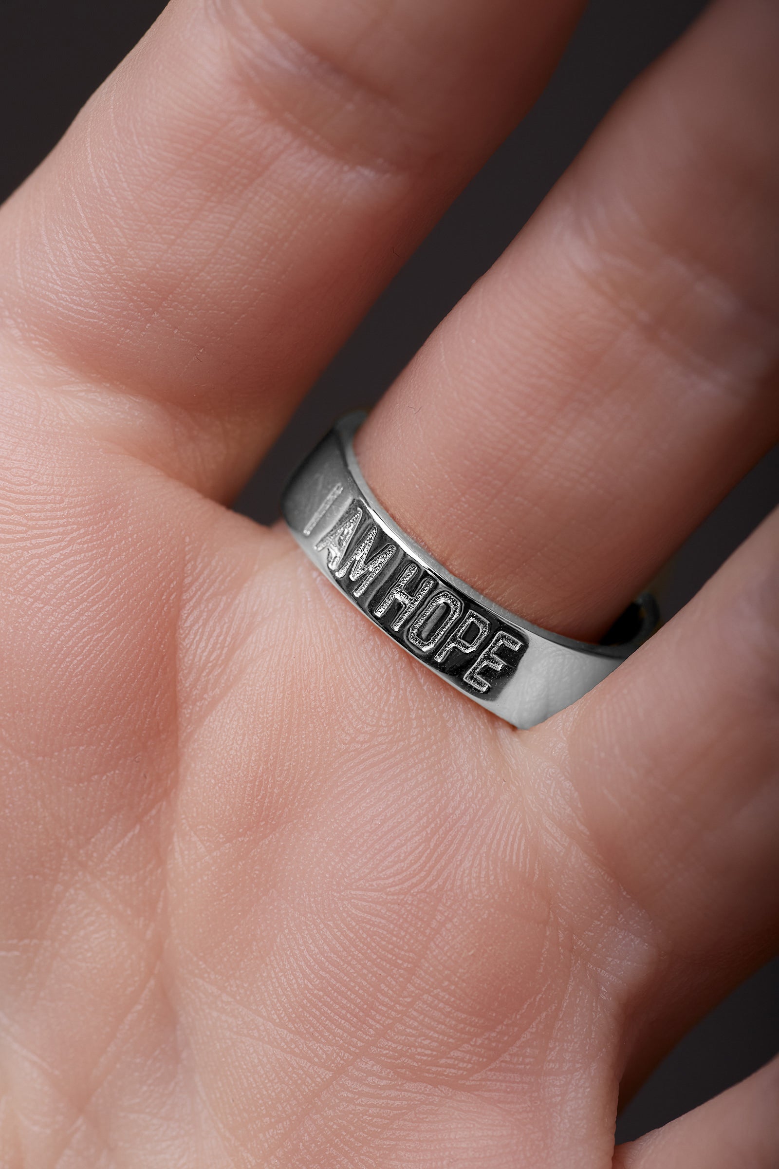 Silver ring with 'I AM HOPE' engraving on a finger against a dark background