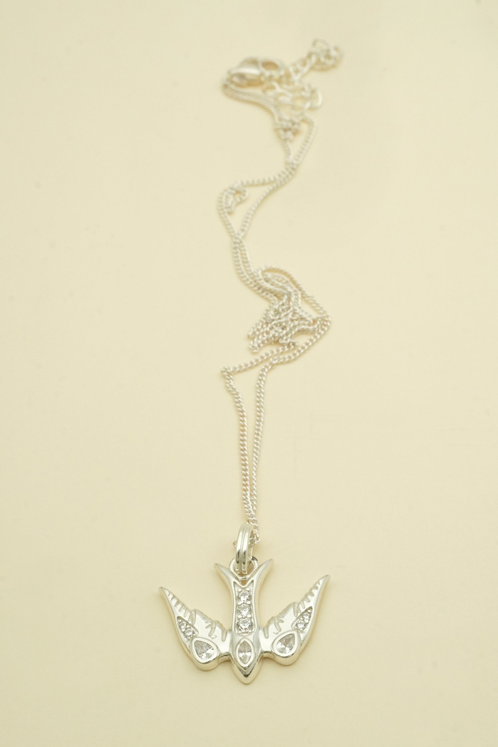 Silver bird necklace with a swallow-shaped pendant on a beige background
