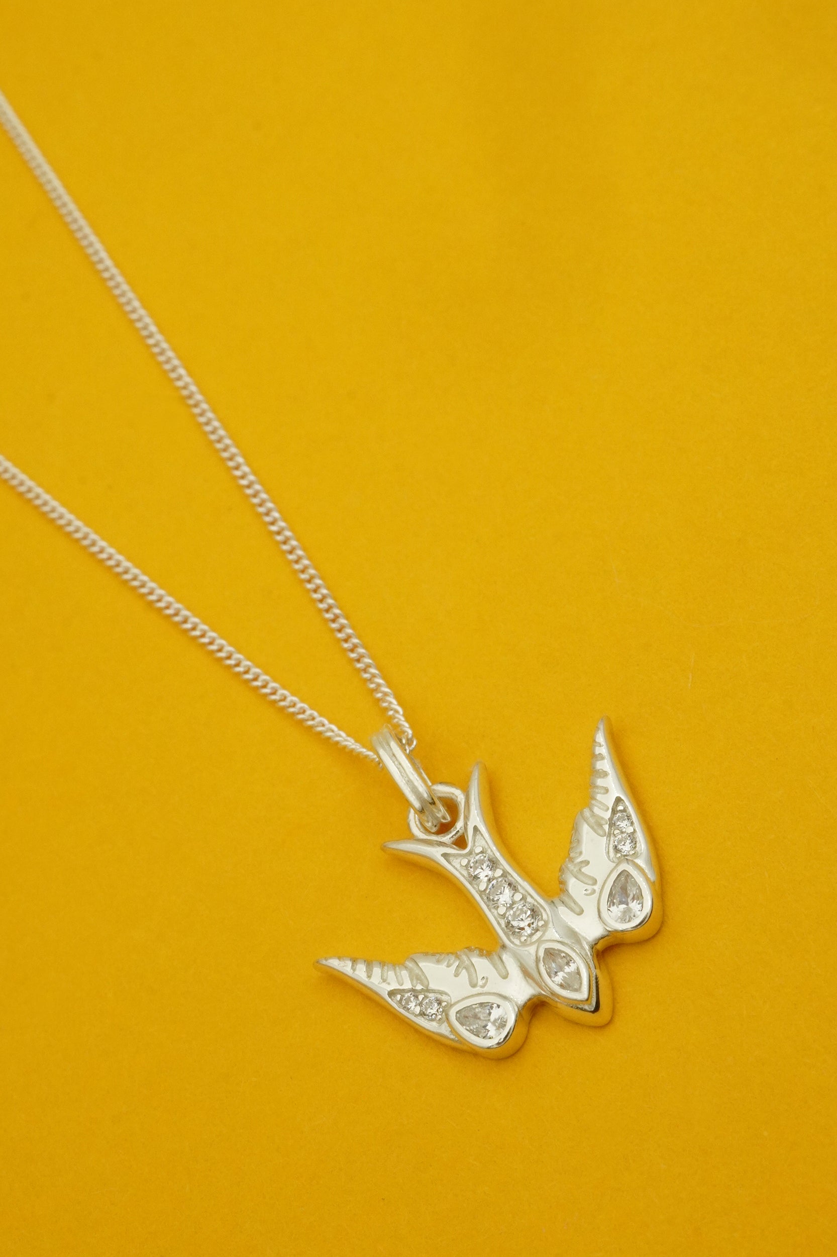Silver swallow-shaped pendant necklace on a chain against an orange background