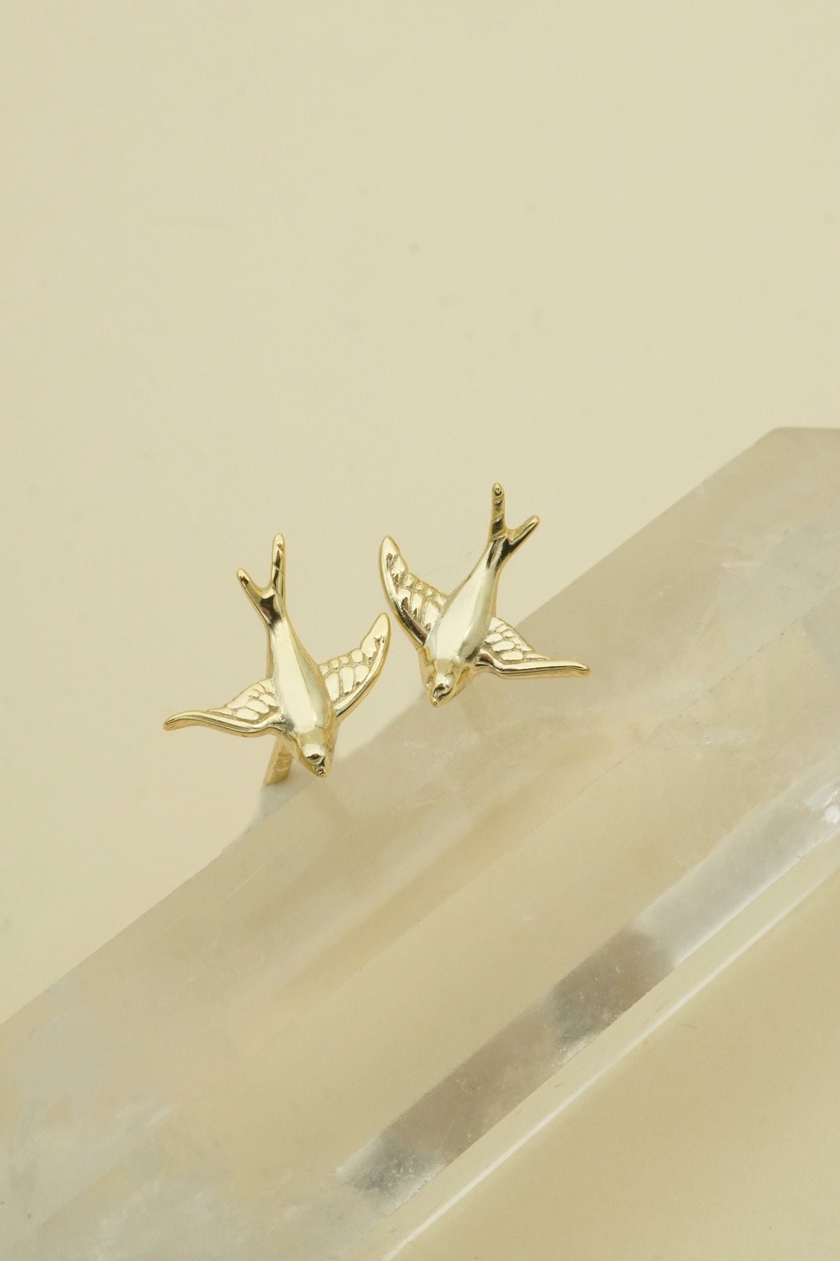 Gold bird-shaped earrings on a beige stone surface