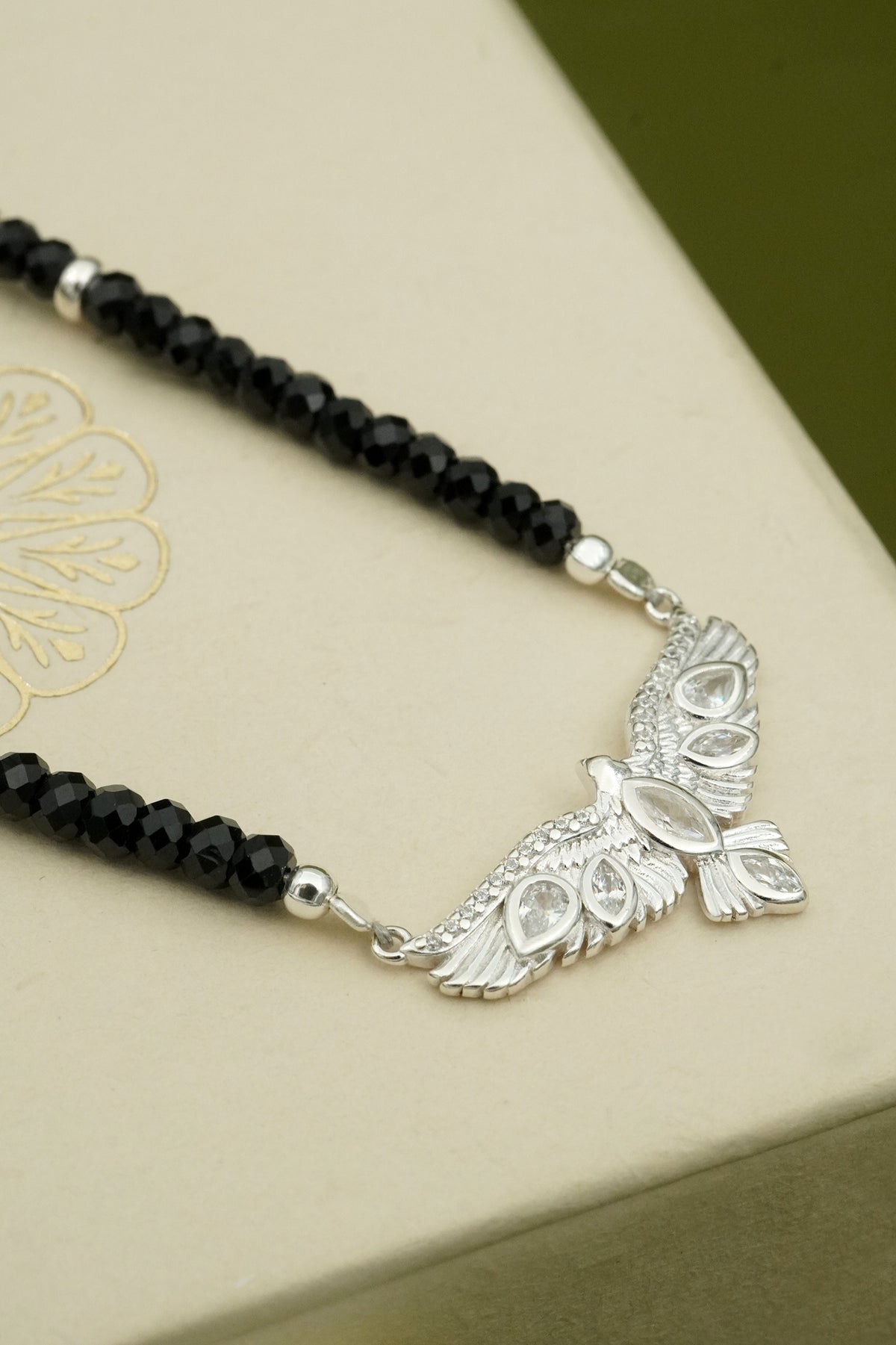 Necklace with black beads and silver hawk pendant on a beige surface
