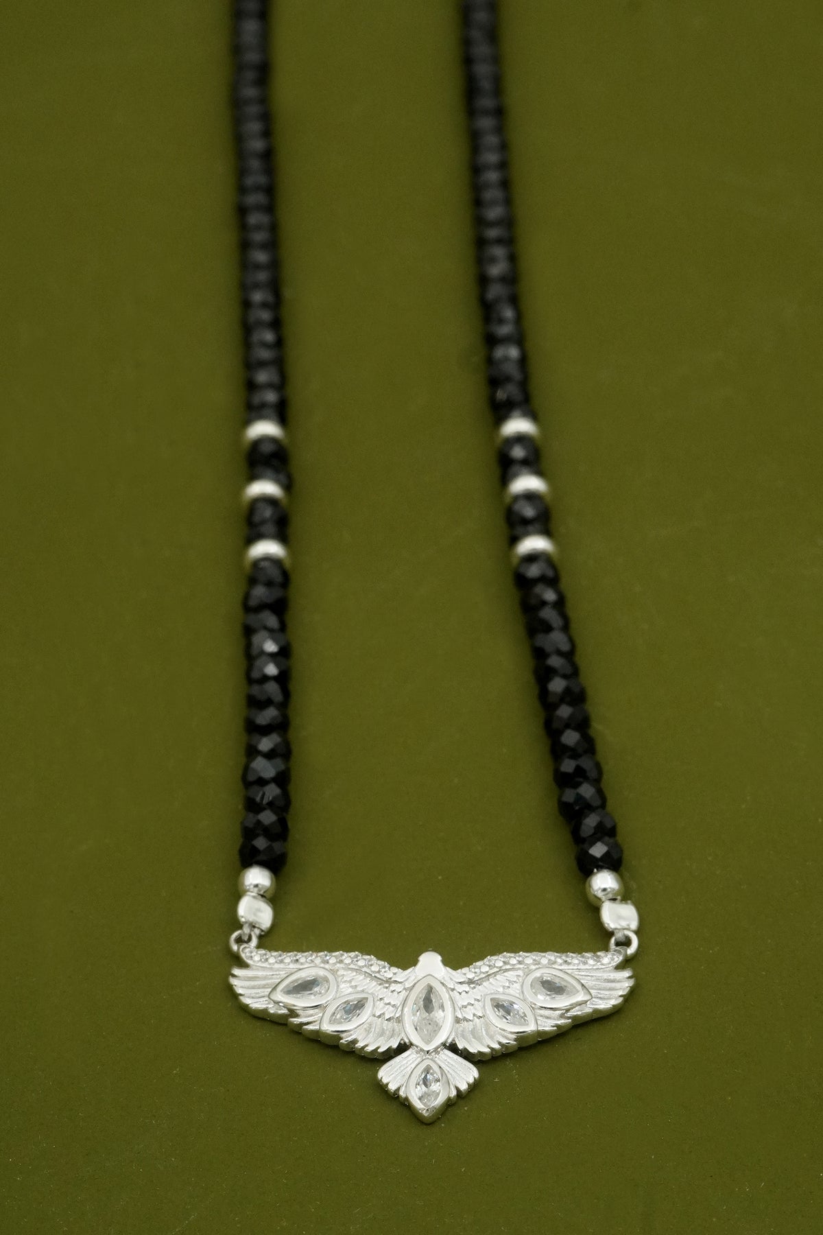 Necklace with black beads and a silver hawk bird with wings on a green background