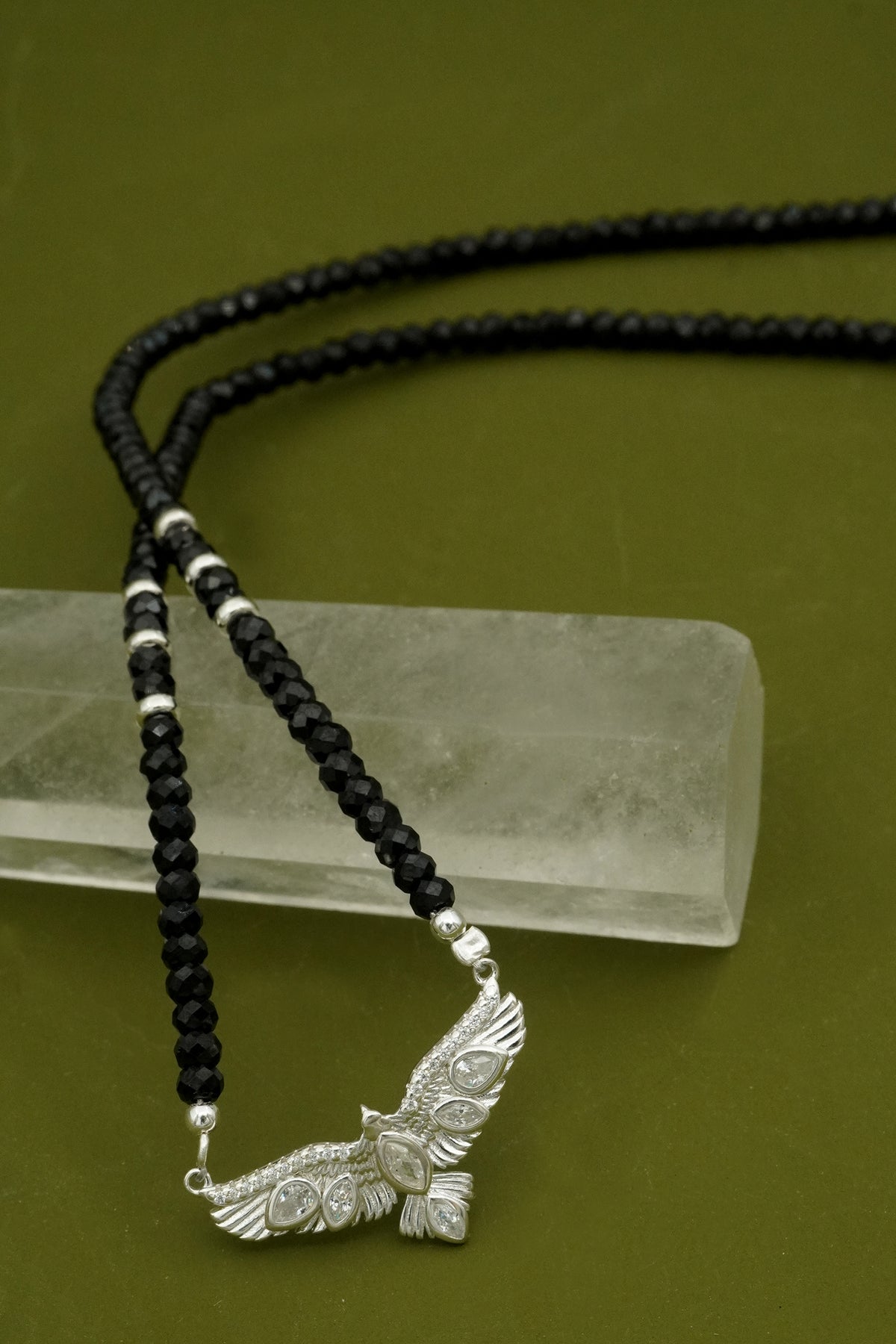 Black beaded necklace with a silver NZ hawk pendant on a green background
