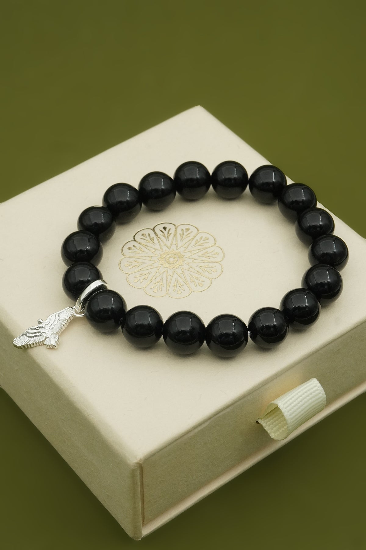 Black agate crystal beaded bracelet with a silver hawk bird charm on a decorative jewellery box