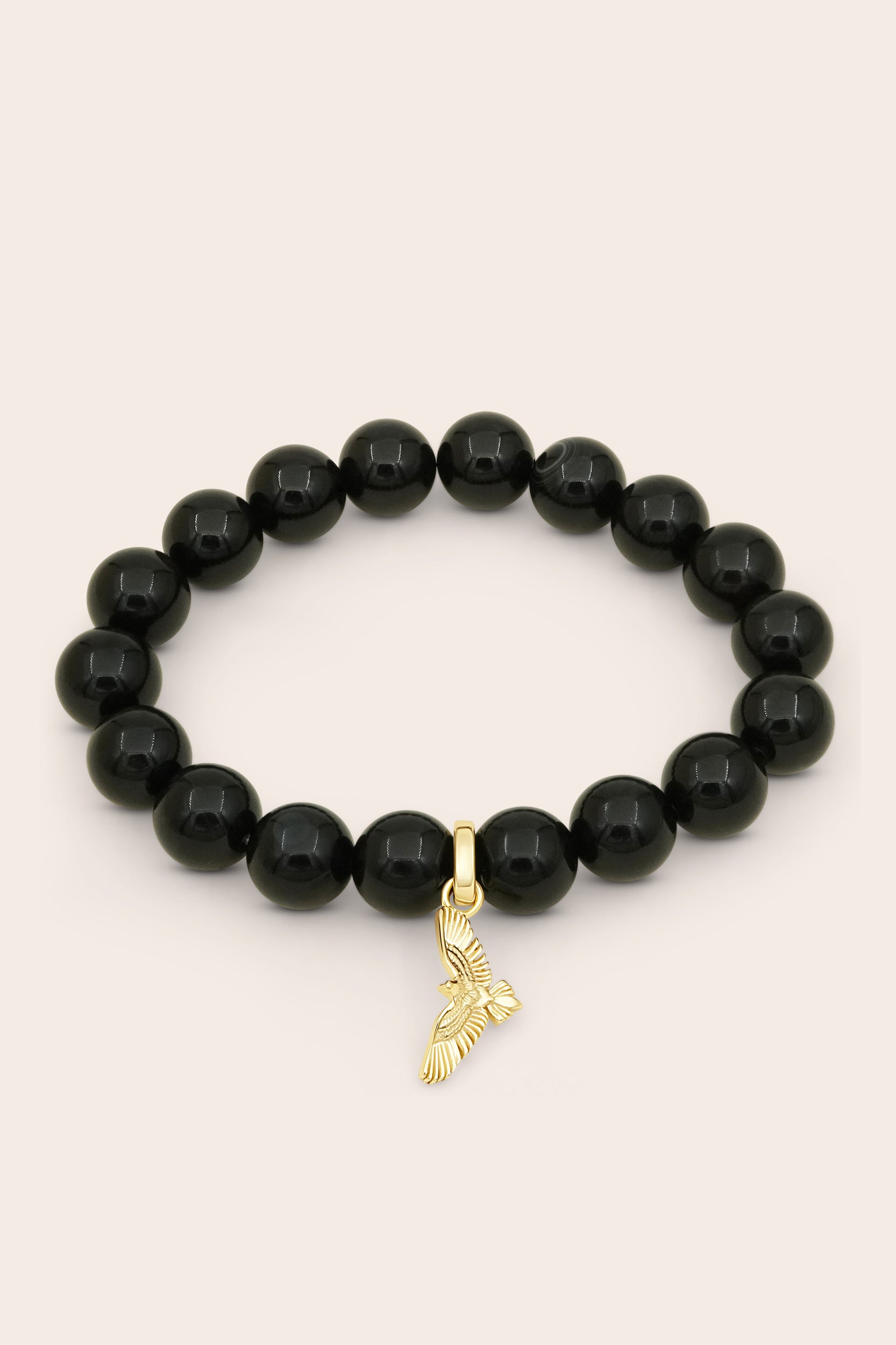Black agate beaded bracelet with a gold soaring hawk bird charm on a beige background