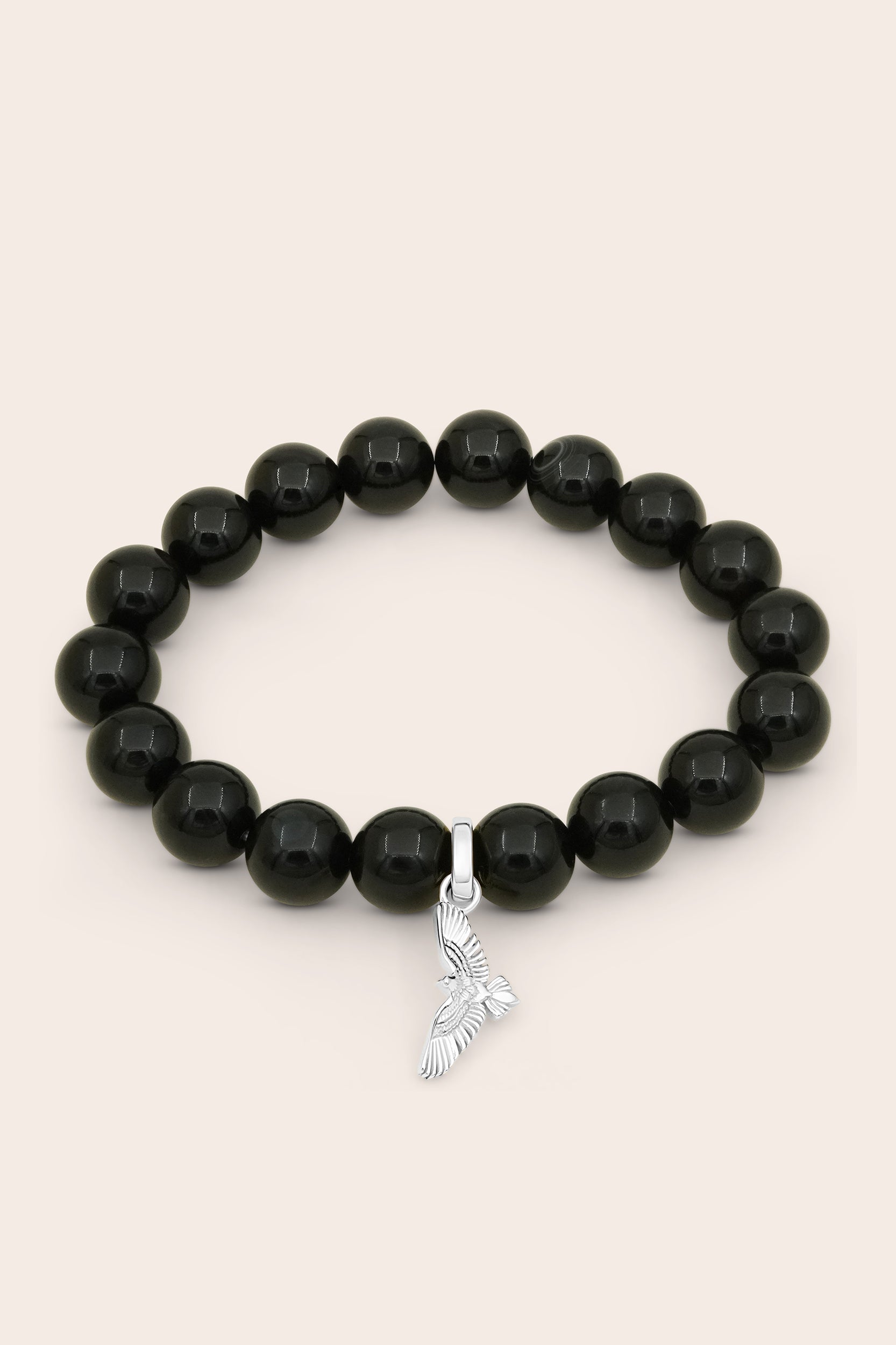 Black agate beaded bracelet with a silver charm on a beige background for protection