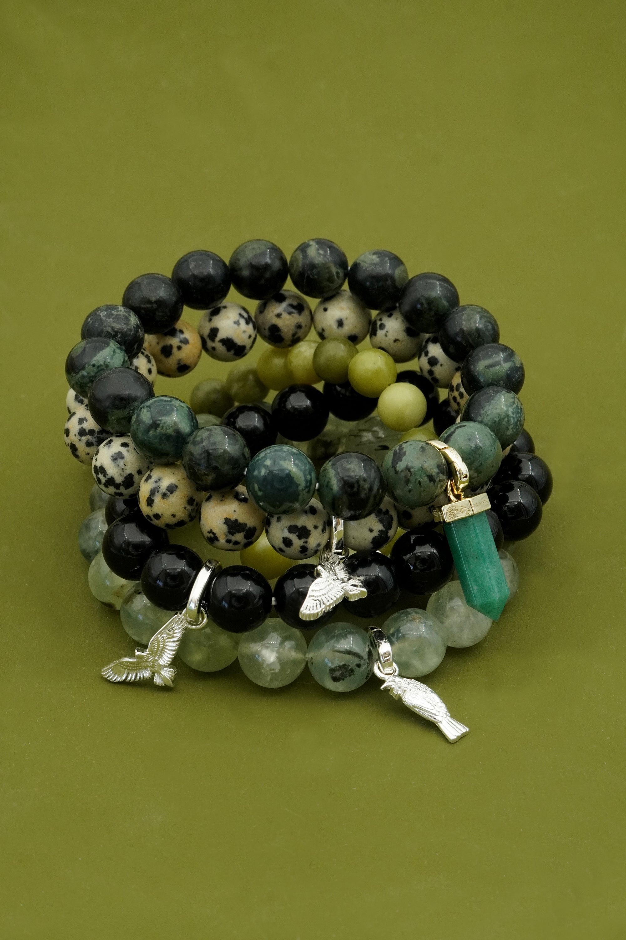 Stack of green gemstone beaded bracelets with silver charms on a green background