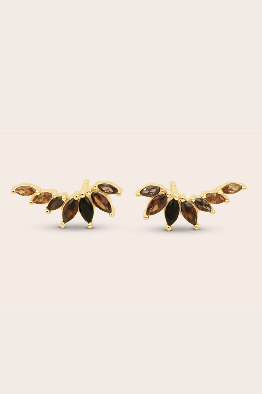 Gold leaf-shaped earrings with brown gemstones on a light beige background