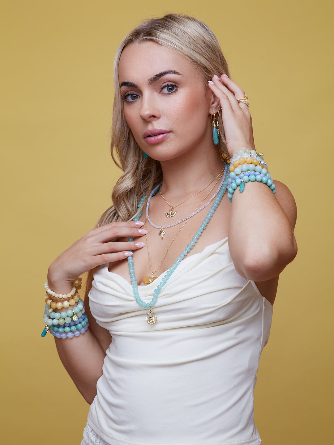 Woman wearing multiple pieces of cloud nine jewellery including a necklace, bracelets, and earrings on a yellow background