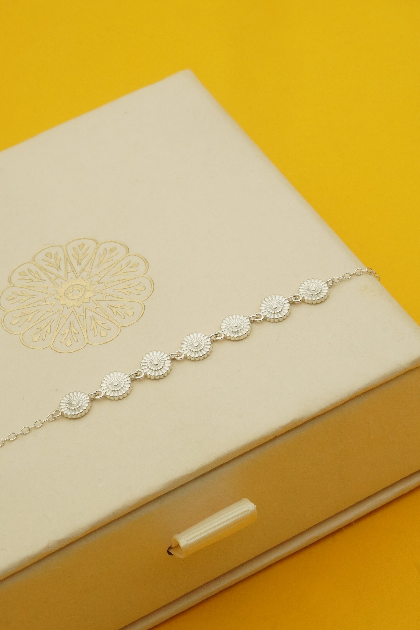 Silver daisy bracelet on a beige cloud nine jewellery box with a yellow background