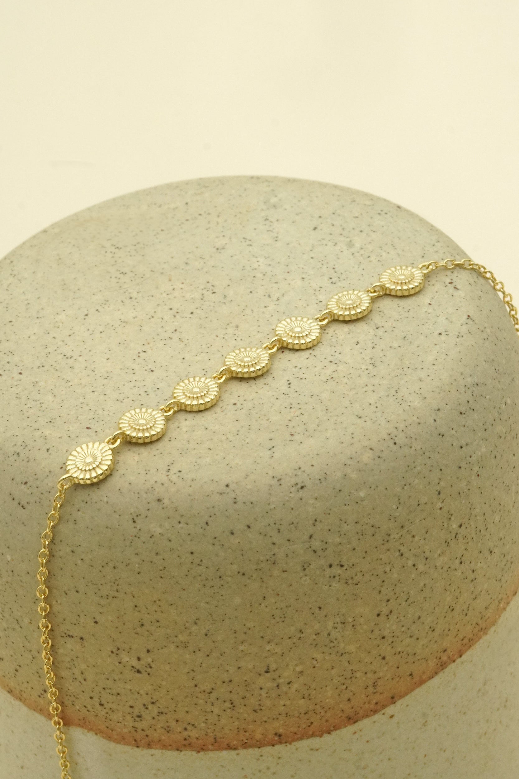 Gold bracelet with sunflower designs on a textured beige surface