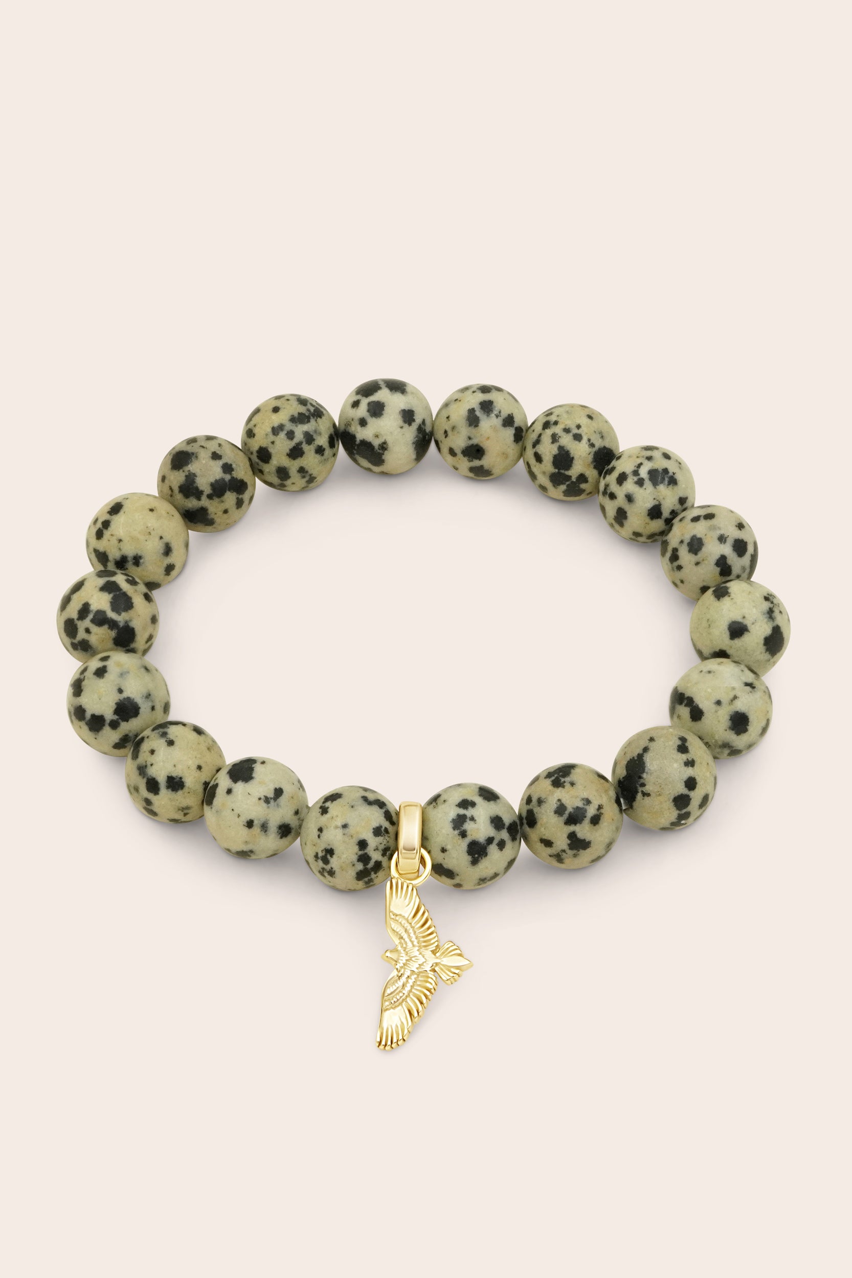 Bracelet with dalmatian jasper beads and a gold soar hawk bird charm on a light pink background