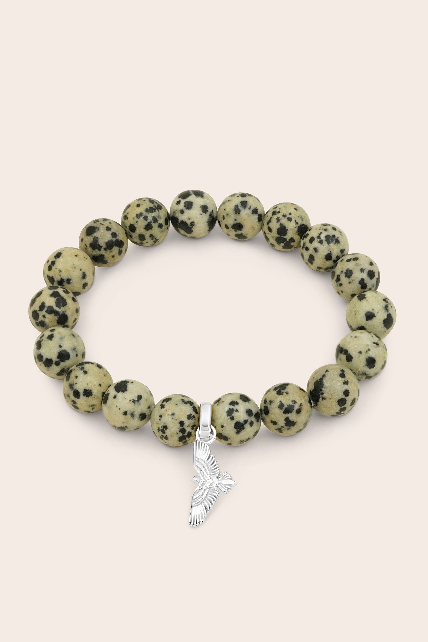 Bracelet with dalmatian jasper beads and a silver hawk bird charm on a beige background