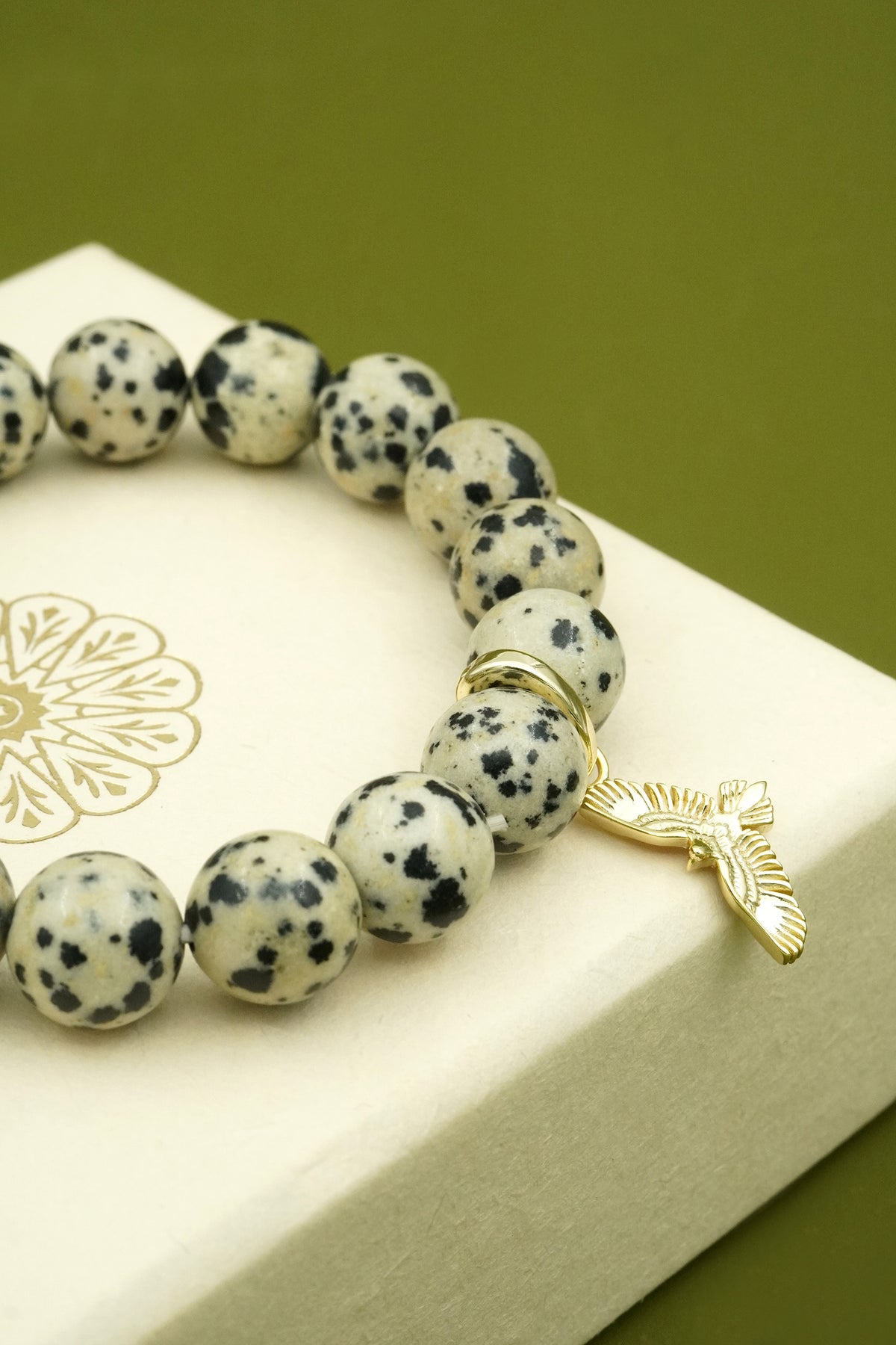 Crystal Bracelet with dalmatian jasper beads and a gold Hawk Eagle charm on a white box with a green background