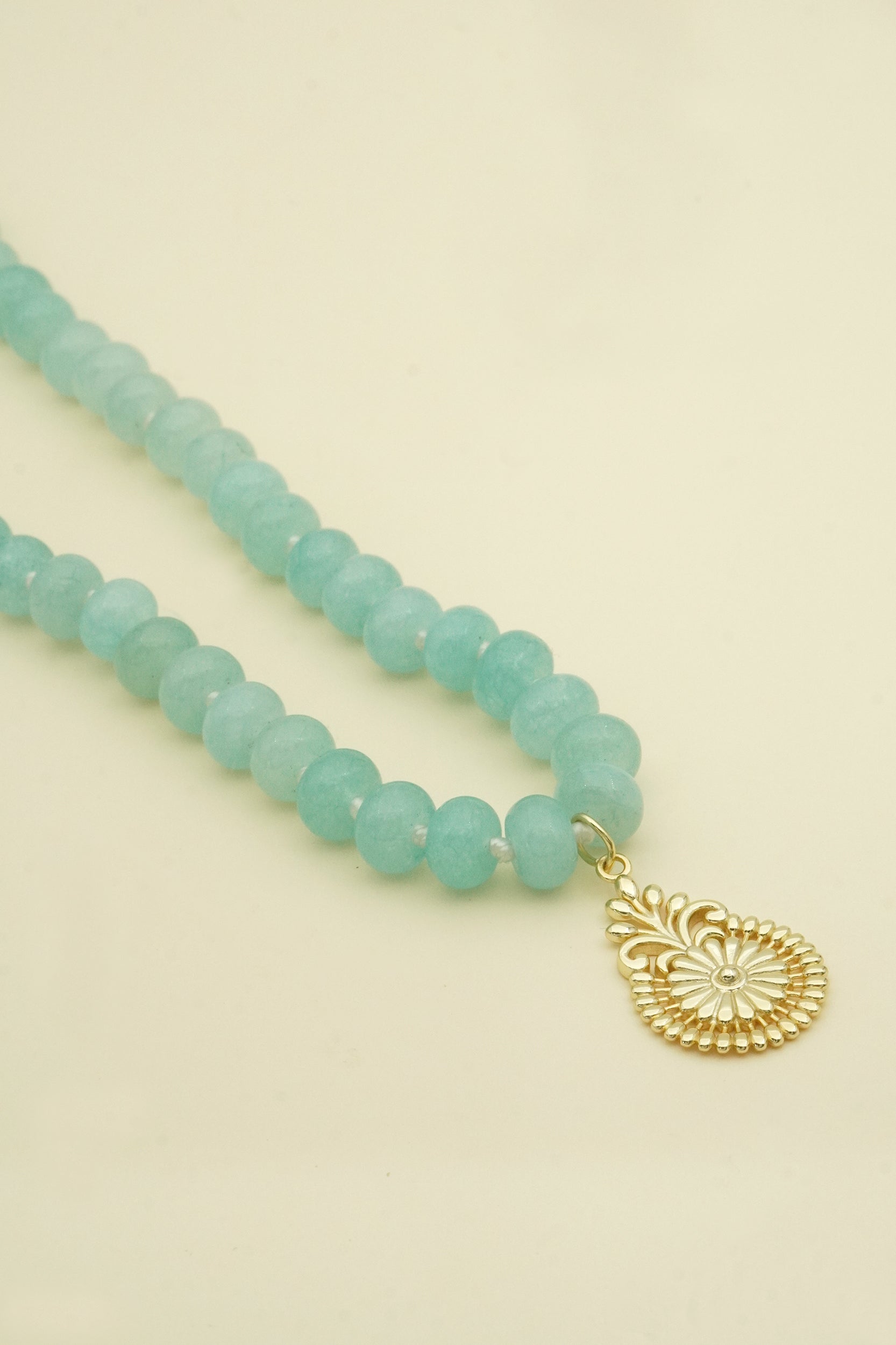 Turquoise aquamarine beaded male necklace with a gold pendant on a beige background