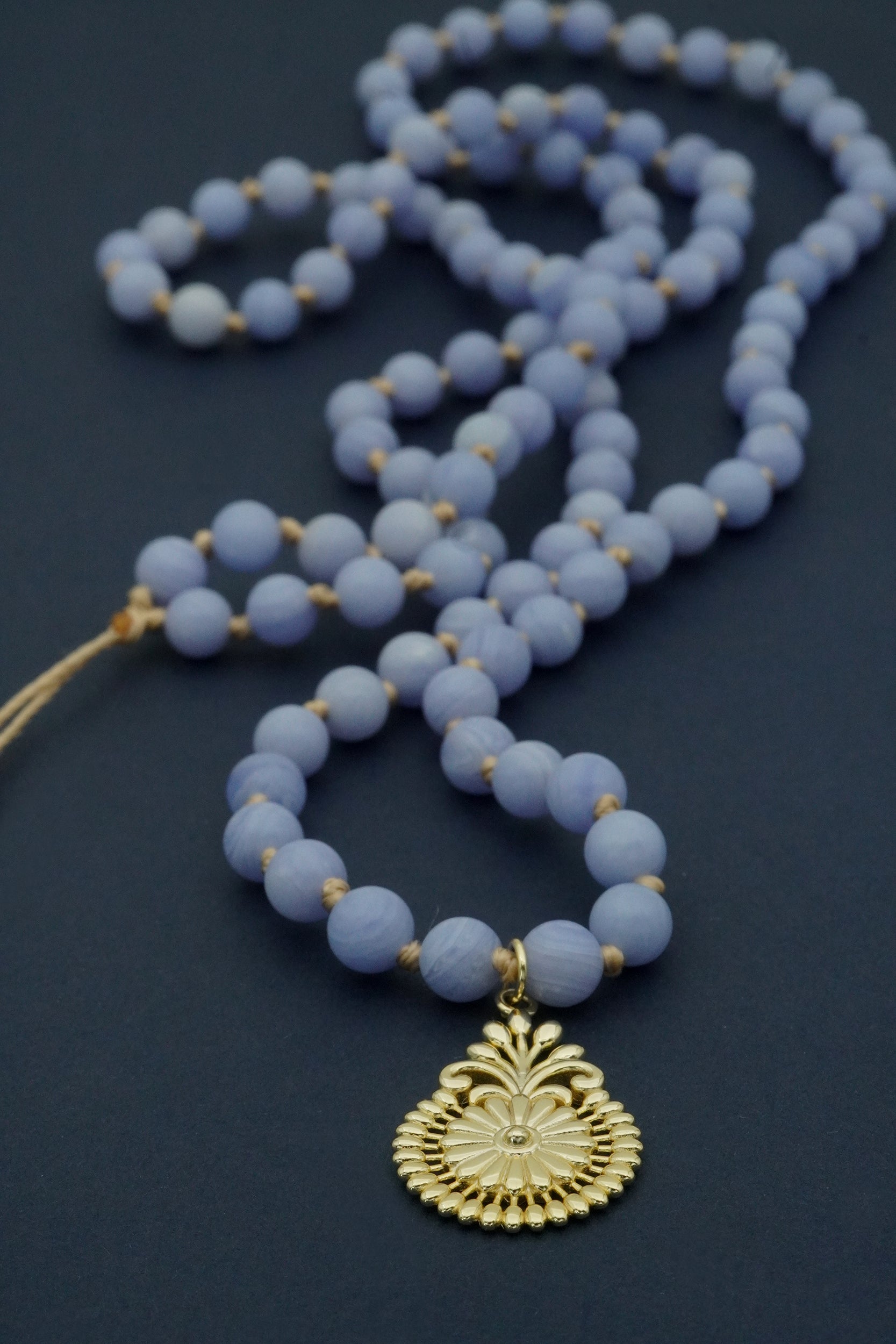 Blue beaded necklace with a gold pendant on a dark background