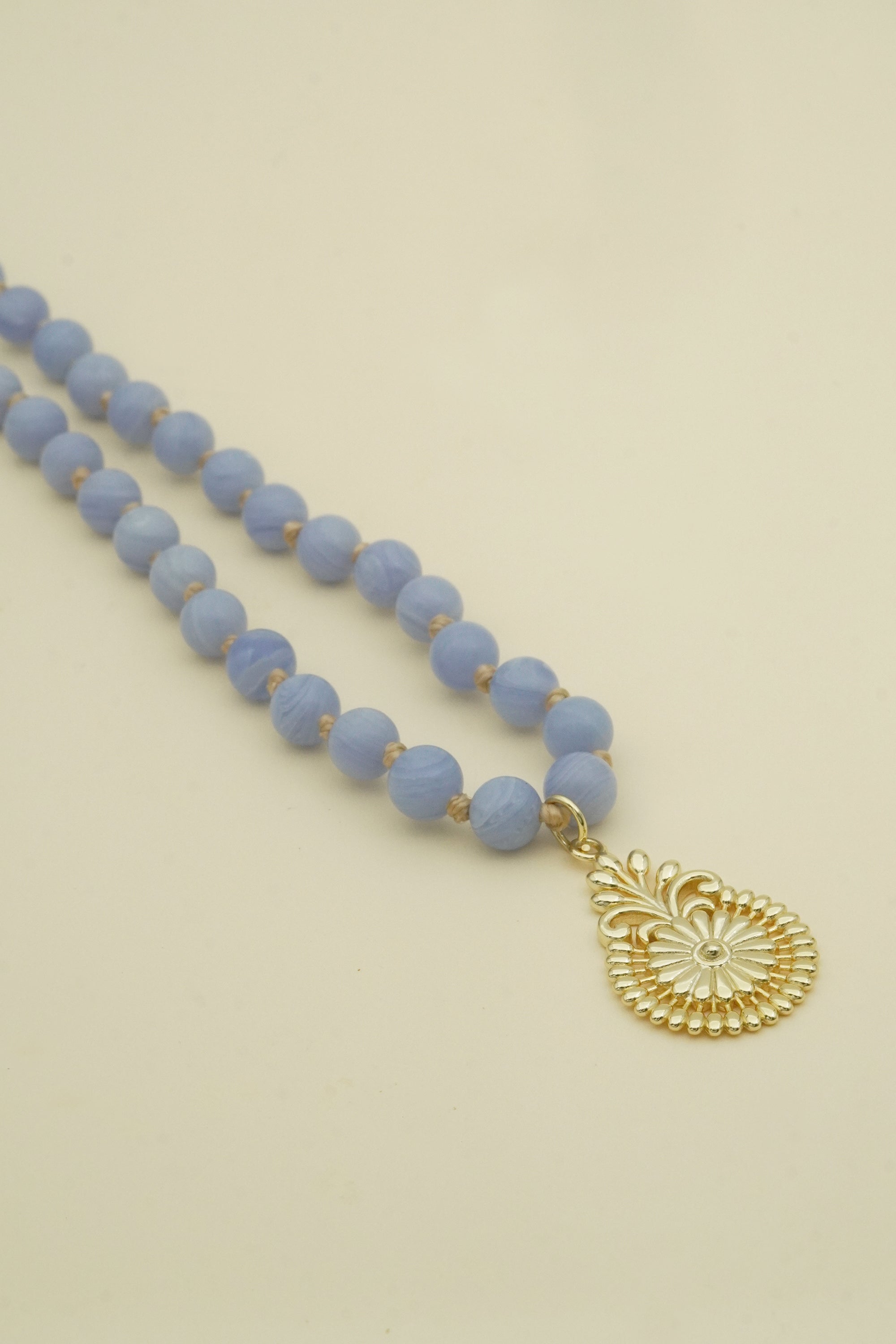 Blue beaded necklace with a gold pendant on a beige background