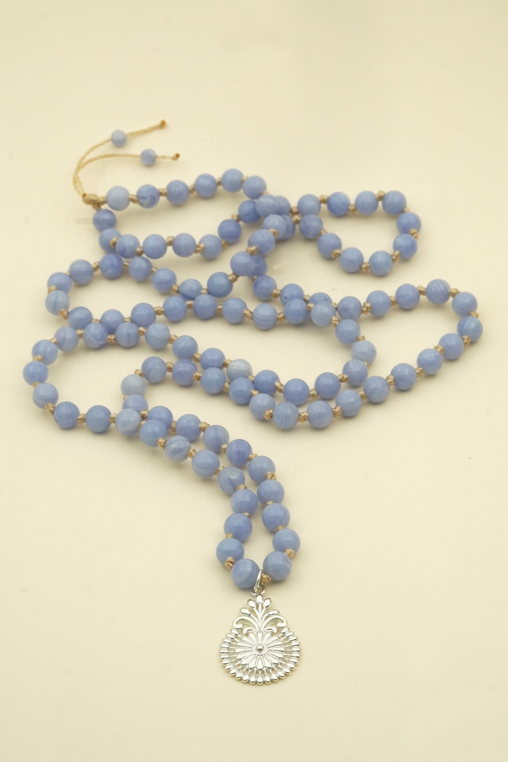 Blue lace agate beaded necklace with a silver pendant on a beige background