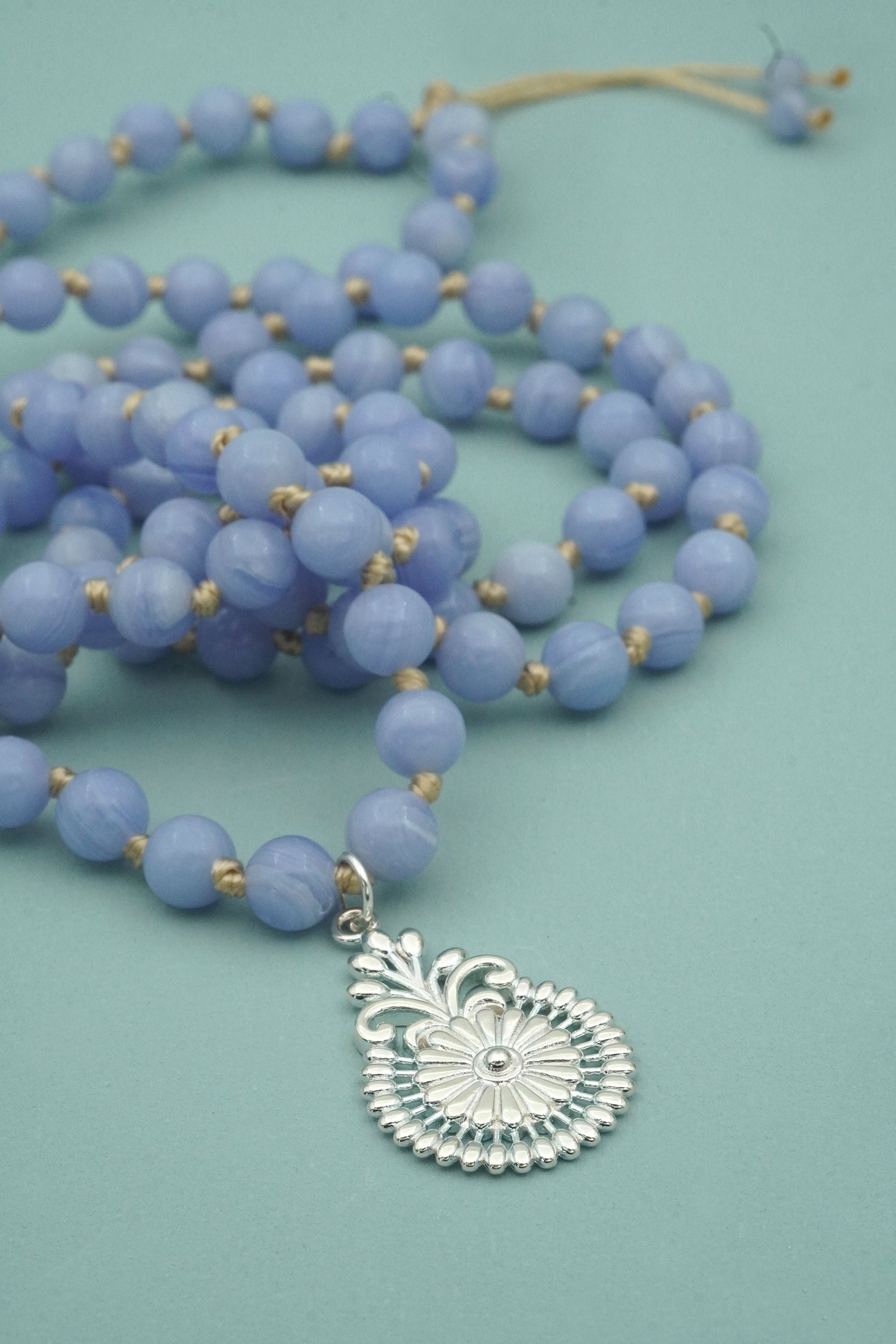 Blue beaded necklace with a silver pendant on a light blue background