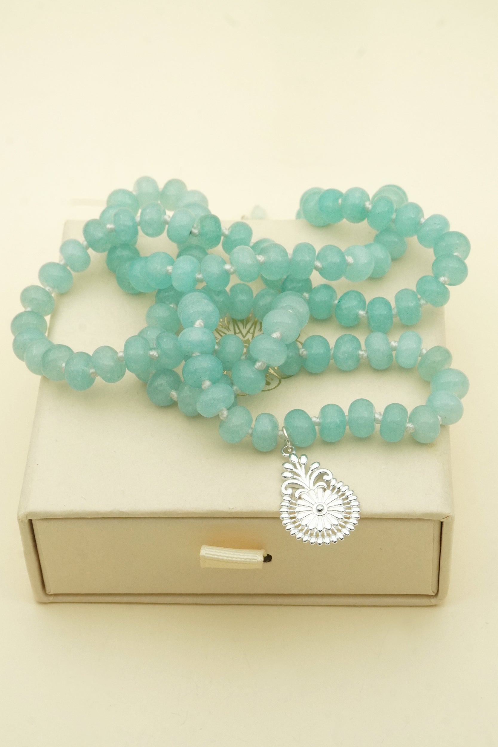 Turquoise crystal beaded necklace with a silver pendant on a beige box