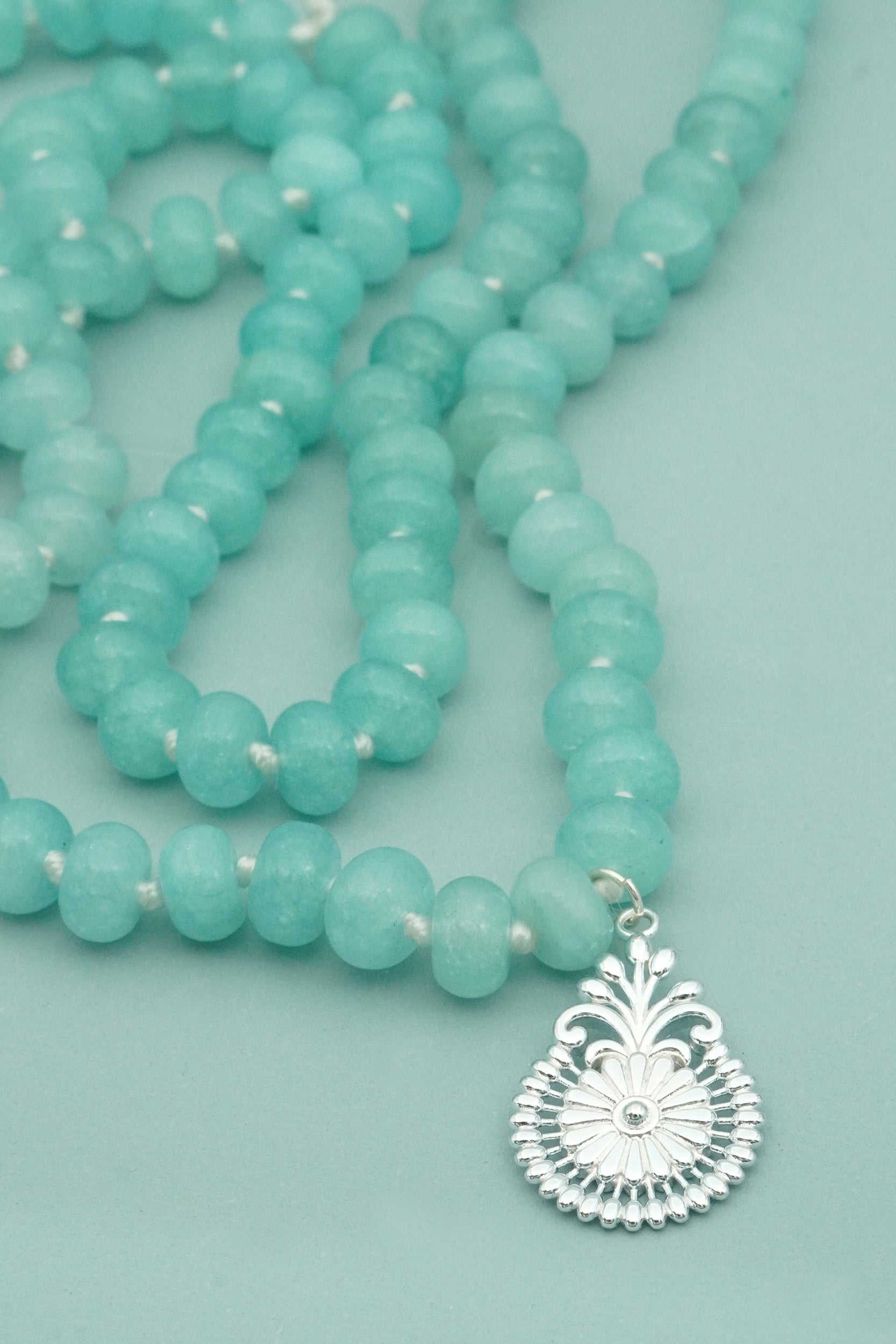 Turquoise beaded male necklace with a silver pendant on a light blue background