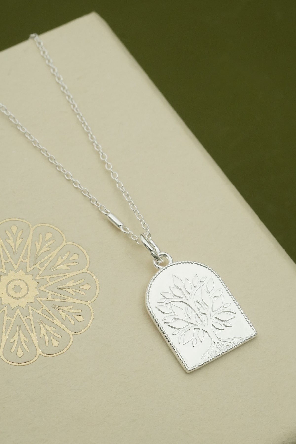 Silver necklace with an embossed tree pendant on a beige surface