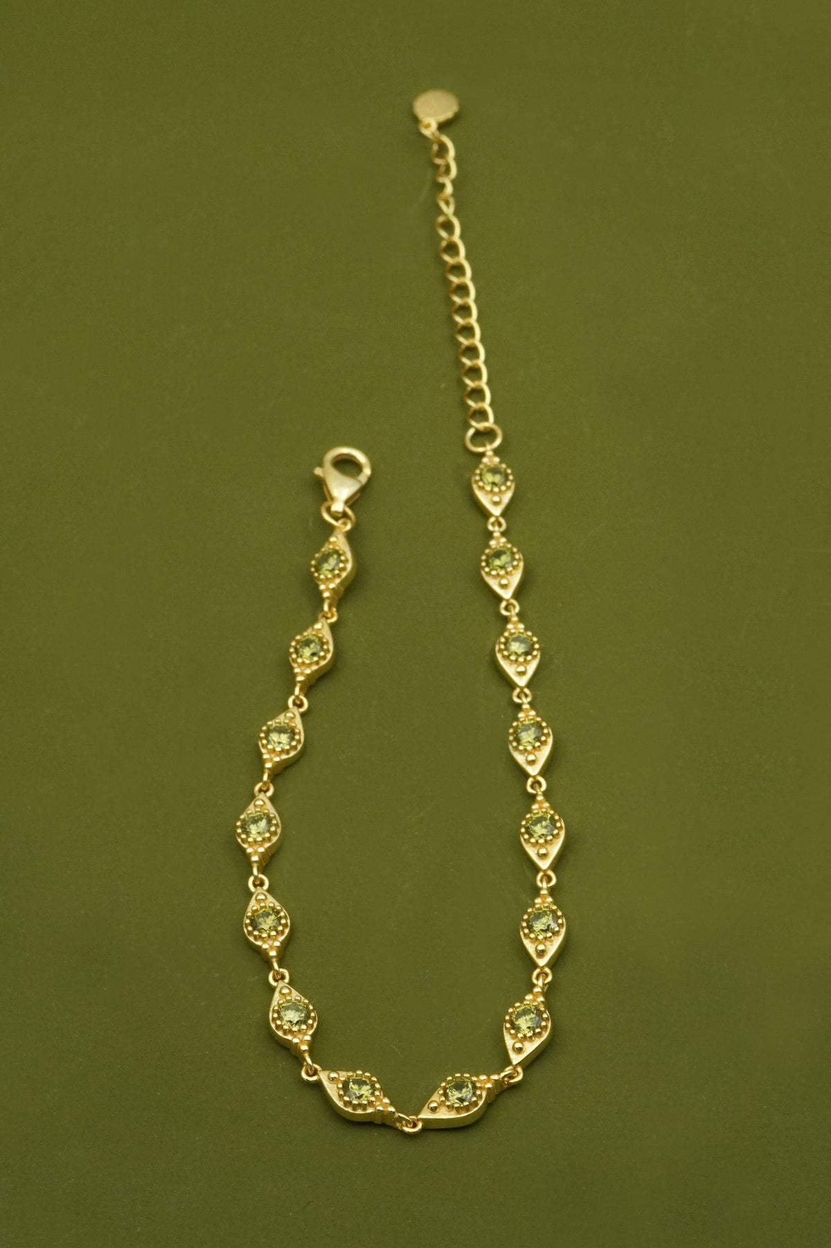 Gold filigree bracelet with green gemstones on a green background