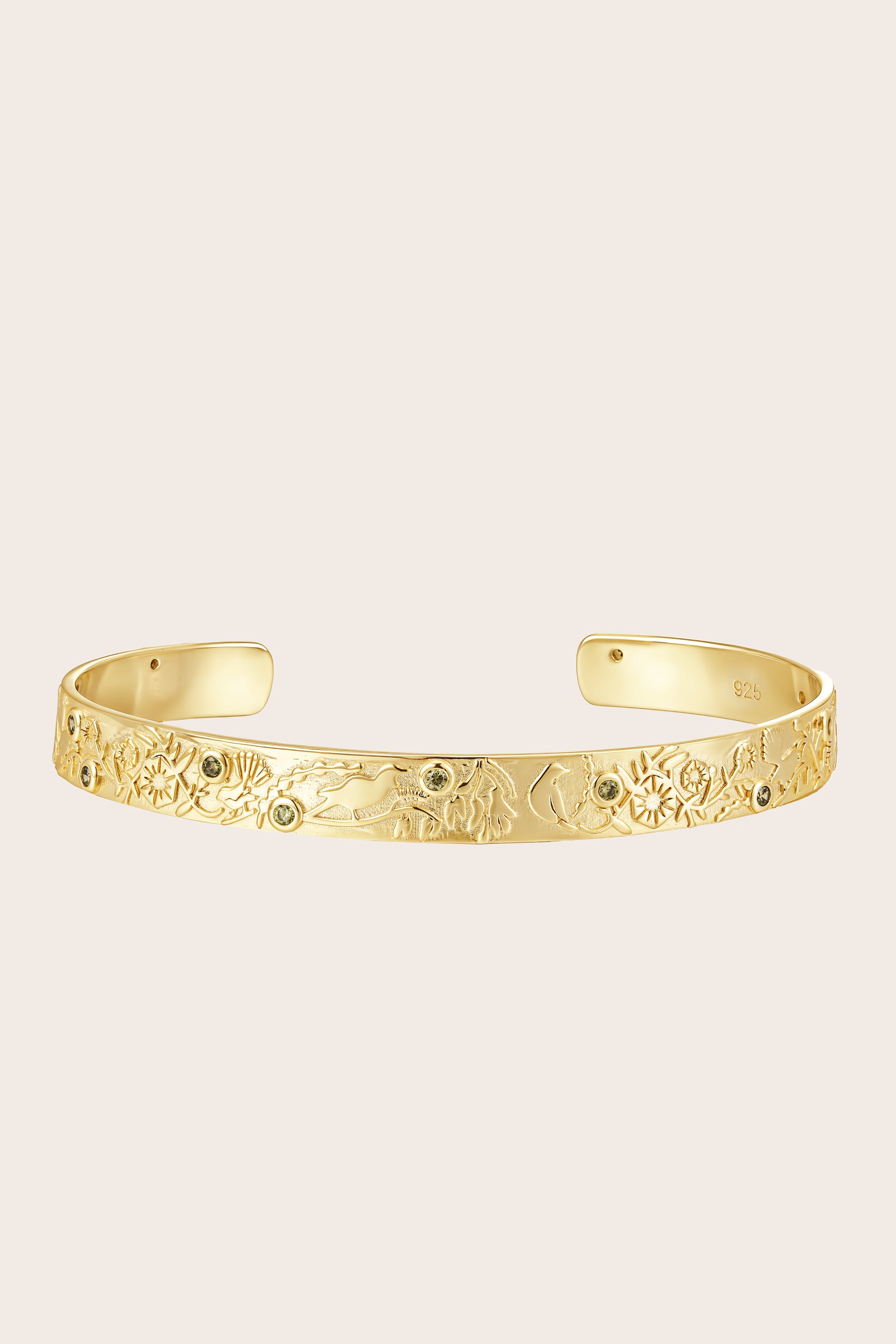 Gold bracelet with intricate forest design and green cubic zirconia on a beige background