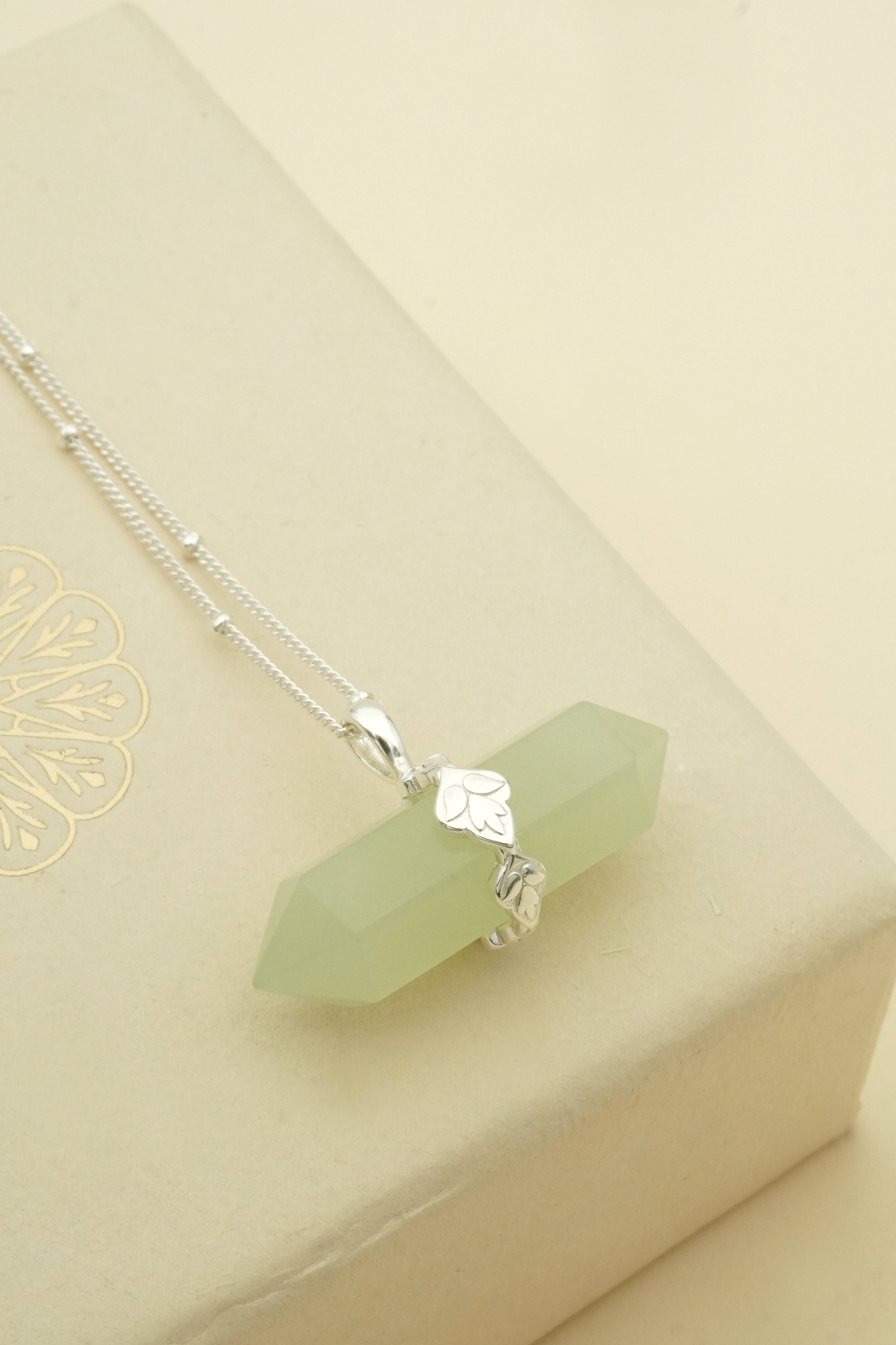 Necklace with a green jade crystal pendant on a beige background