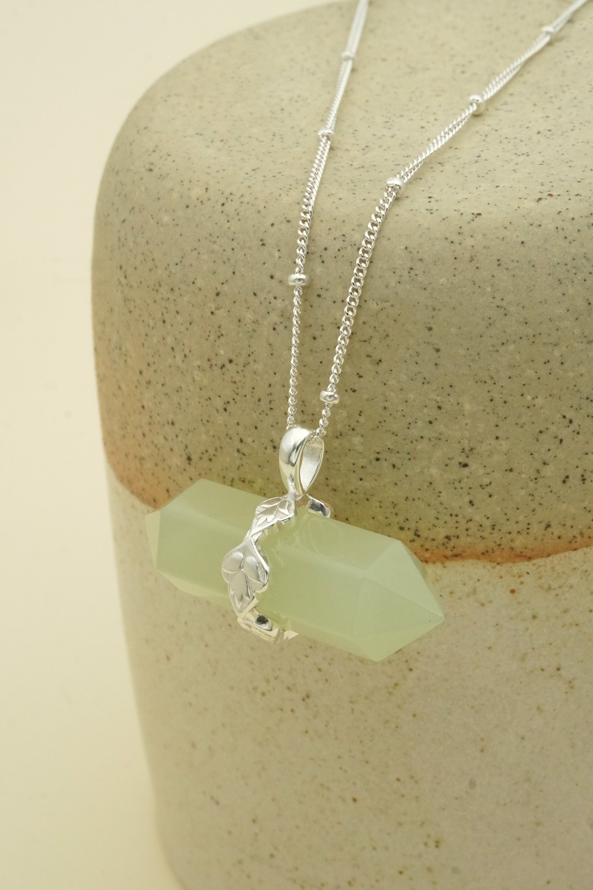Necklace with a green stone pendant on a beige stone surface