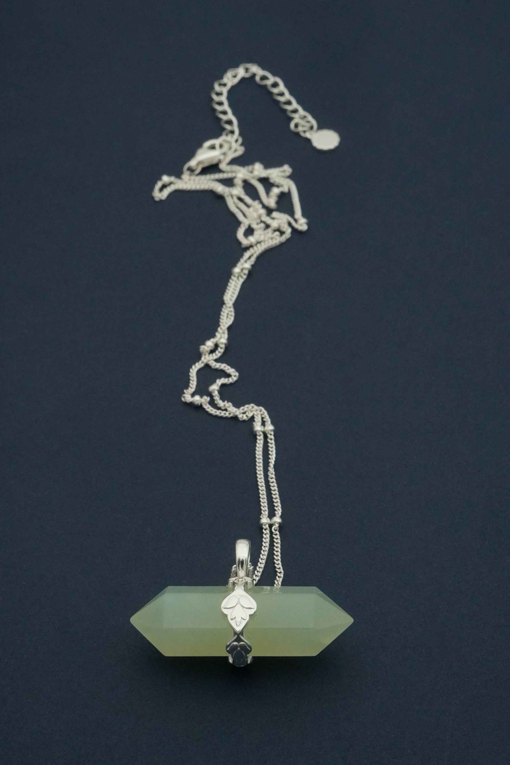 Necklace with a green pendant and silver chain on a dark background