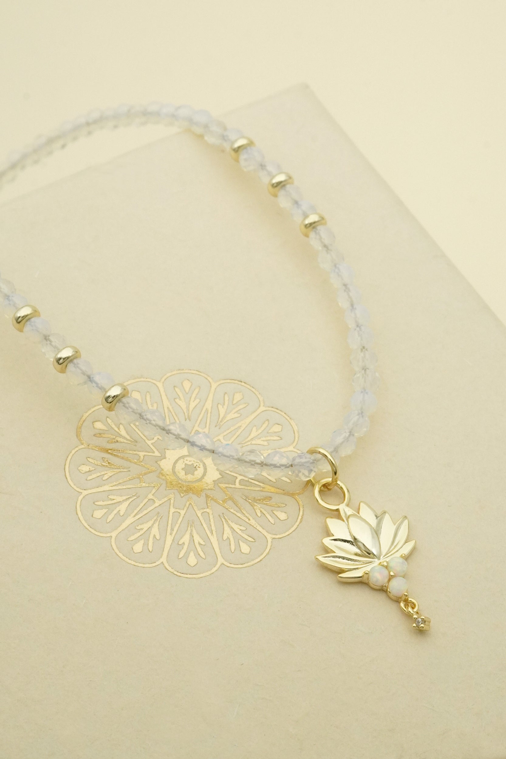 Necklace with gold lotus charm and leaf design on a beige background