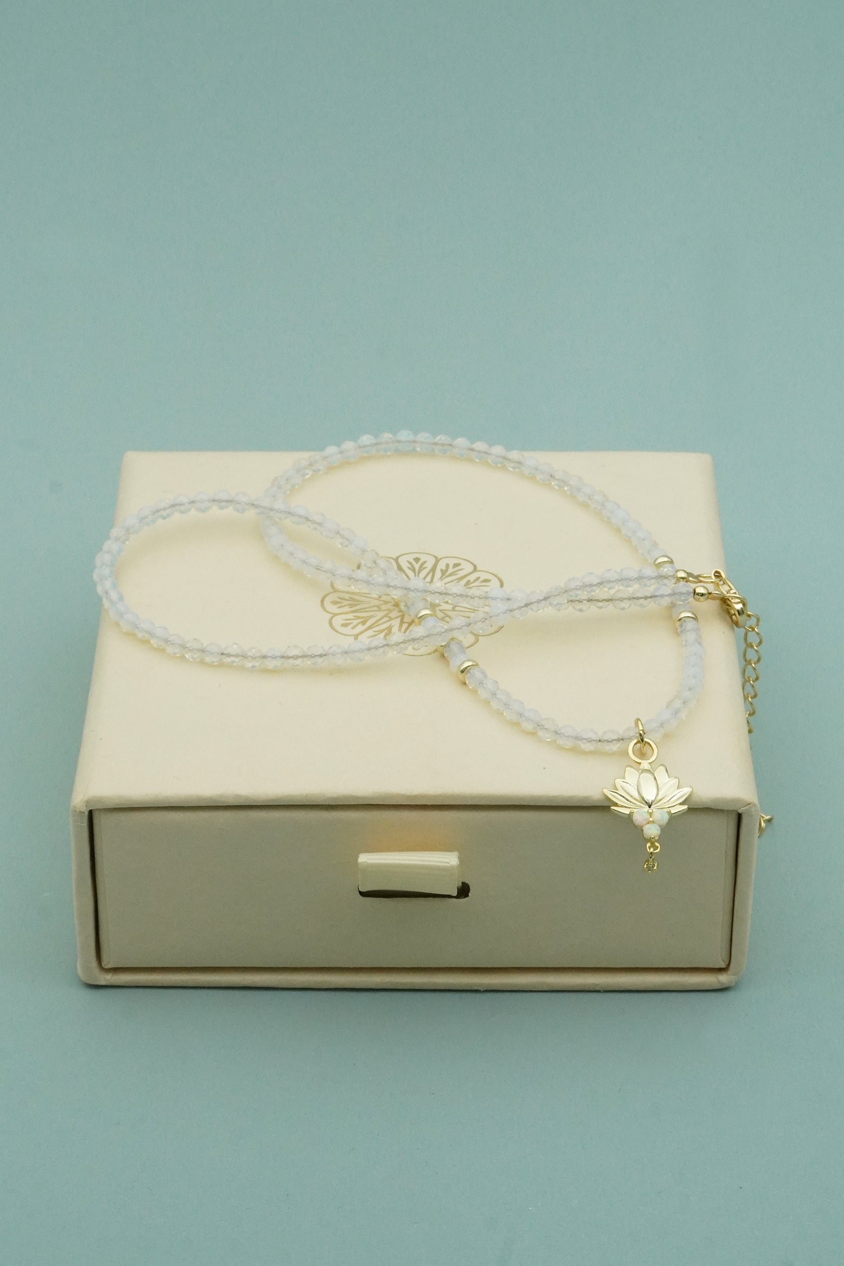 opal necklace with a gold charm on a beige box against a light blue background