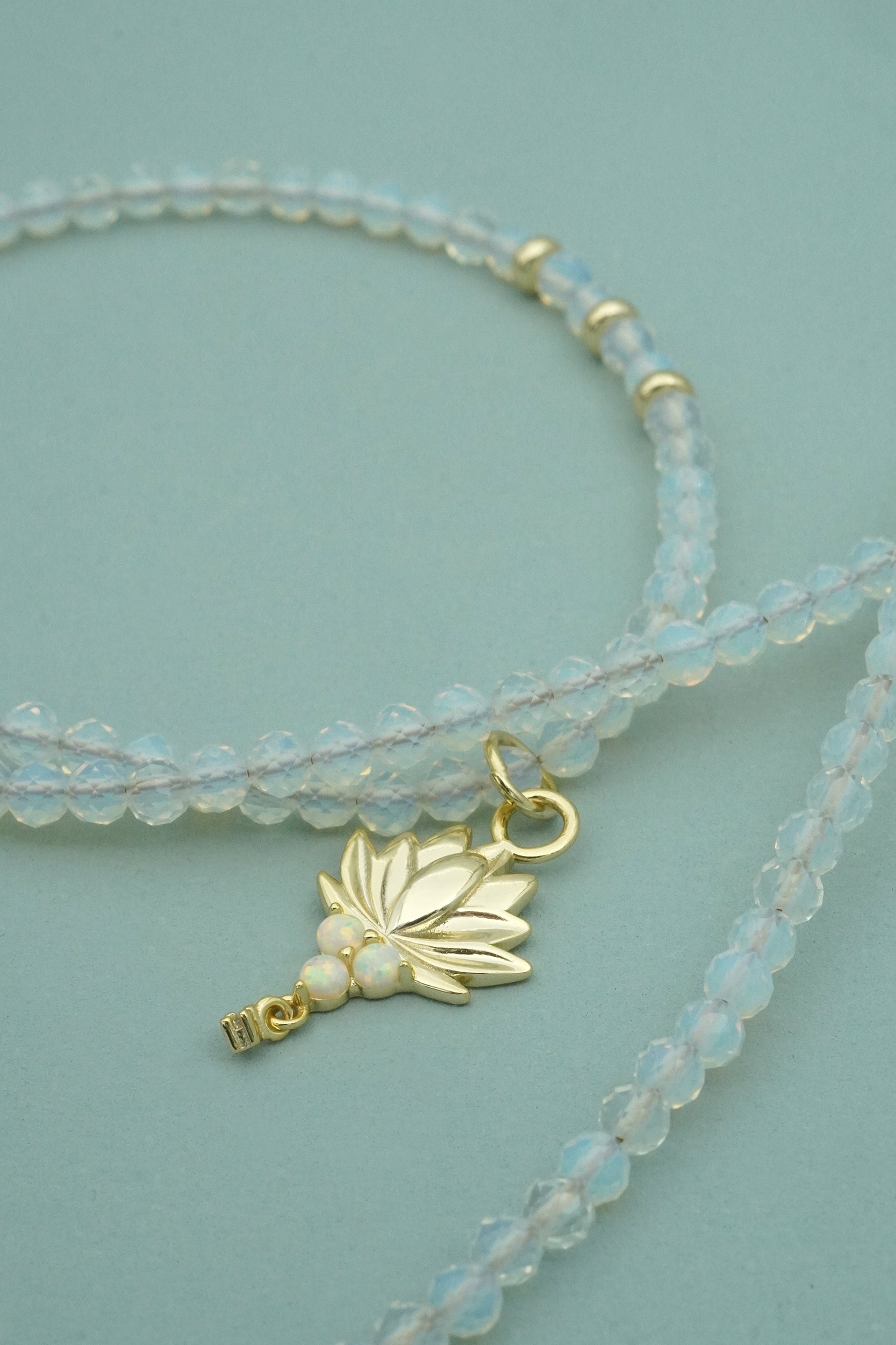 Gold Lotus Necklace with opal beads and gold lotus charm on a light blue background