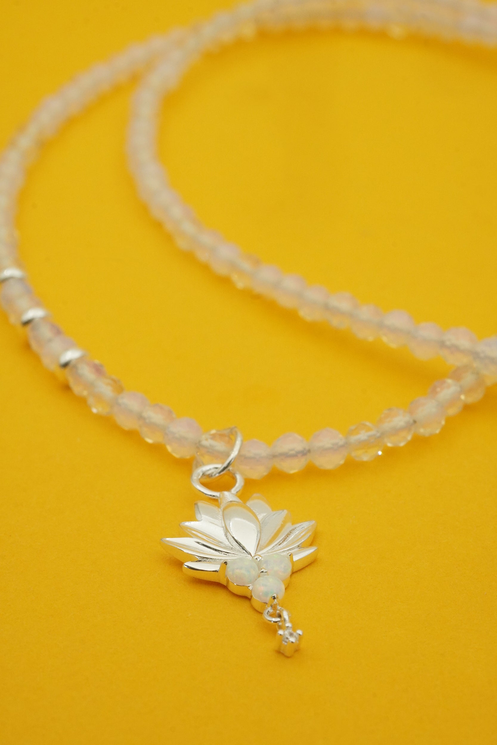 Necklace with a silver lotus flower charm on a yellow background