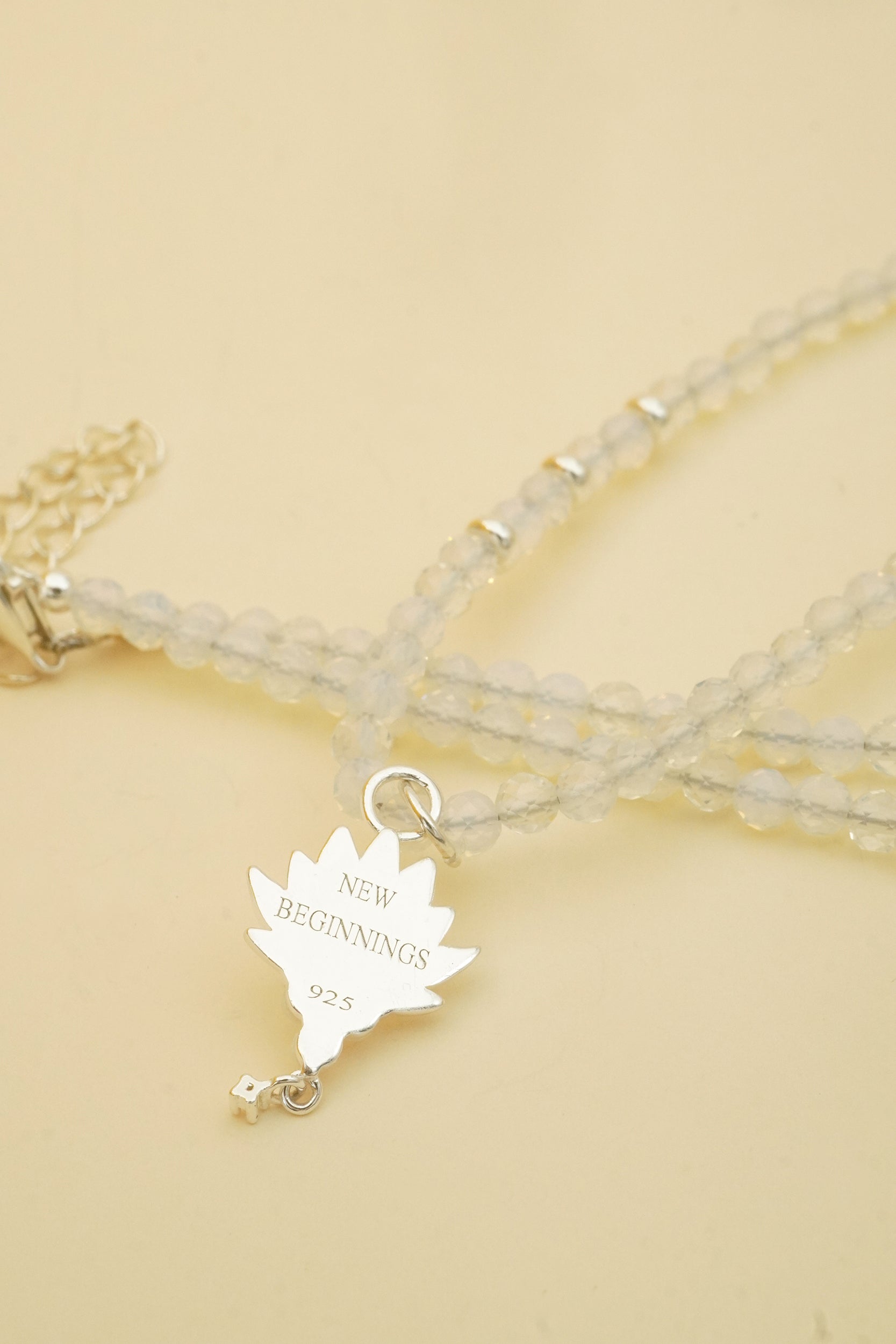 Necklace with a silver lotus charm labeled 'New Beginnings' on a beige background