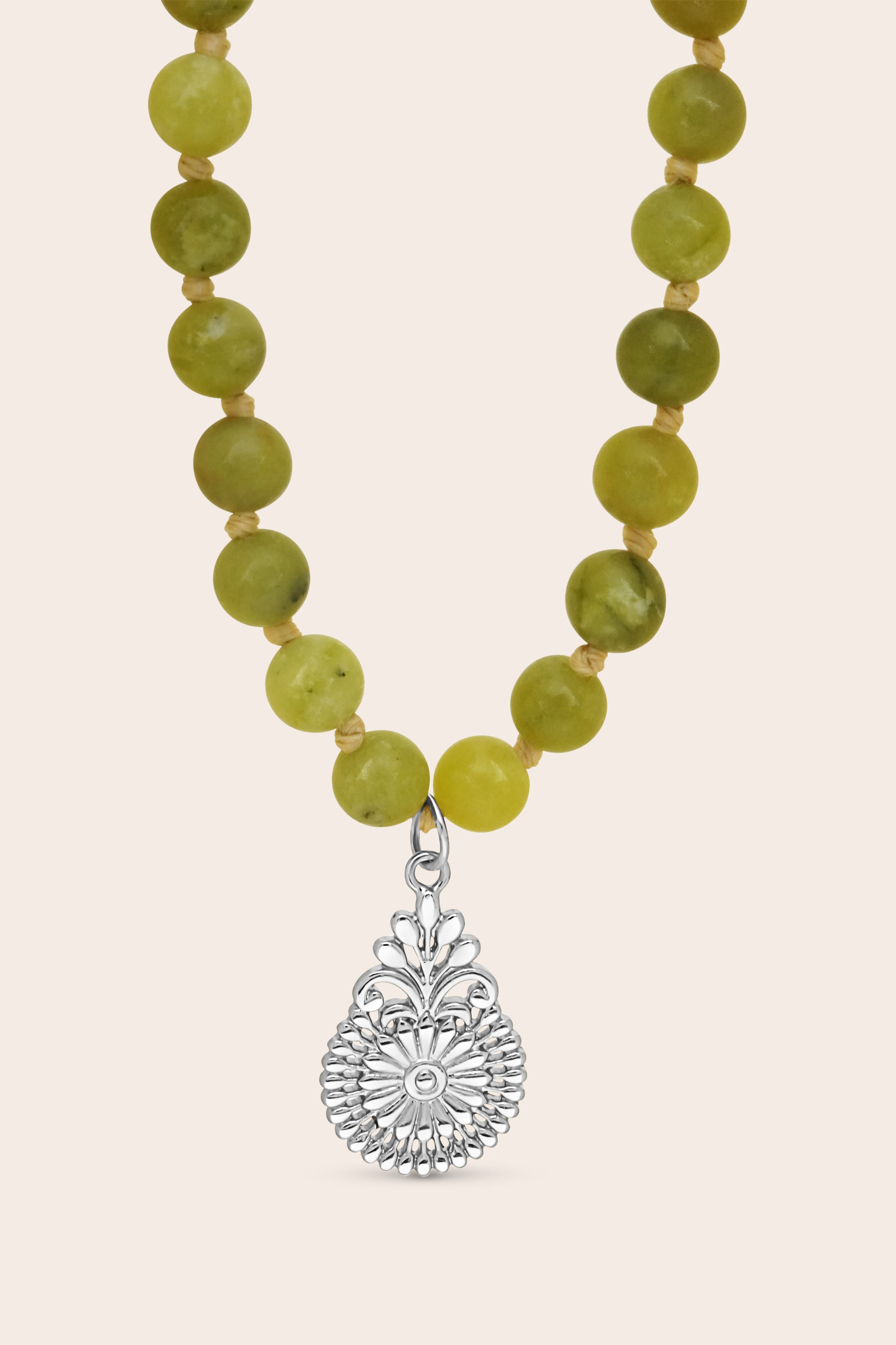 Mala Necklace with green beads and a silver flower pendant on a beige background