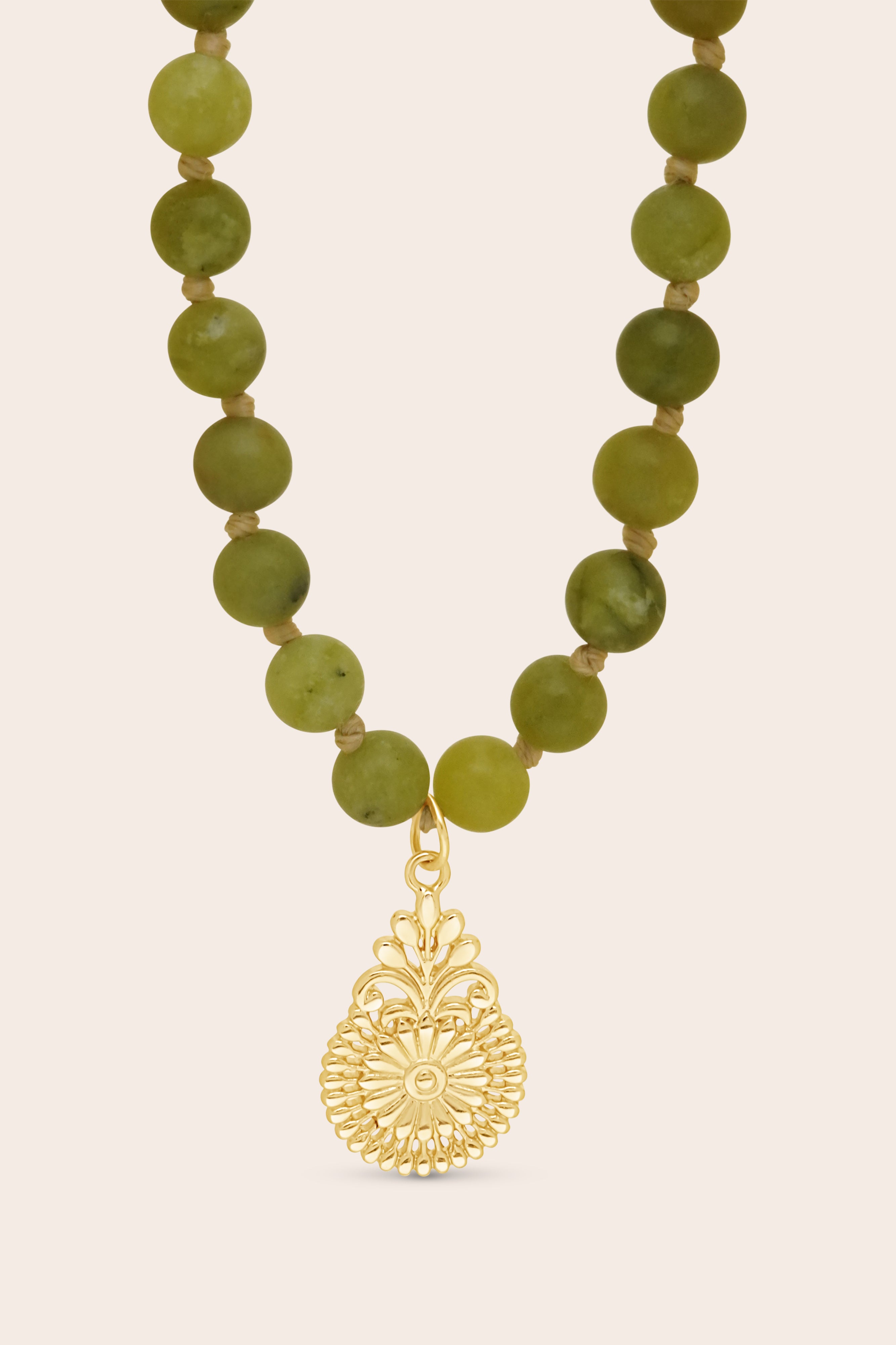 Mala Necklace with green beads and a gold flower pendant on a beige background