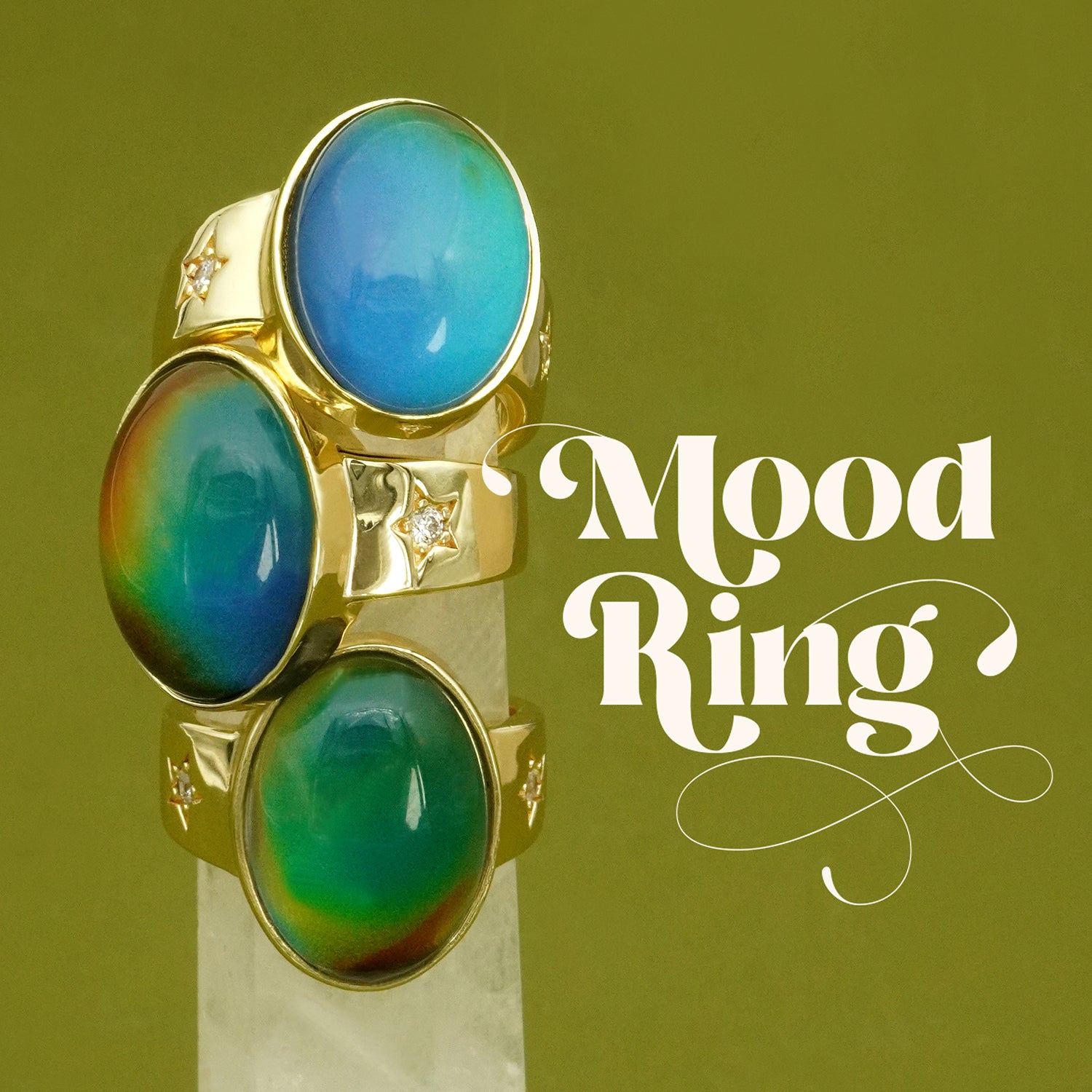 Gold mood ring with blue and green gemstones on a green background, labeled 'Mood Ring'.