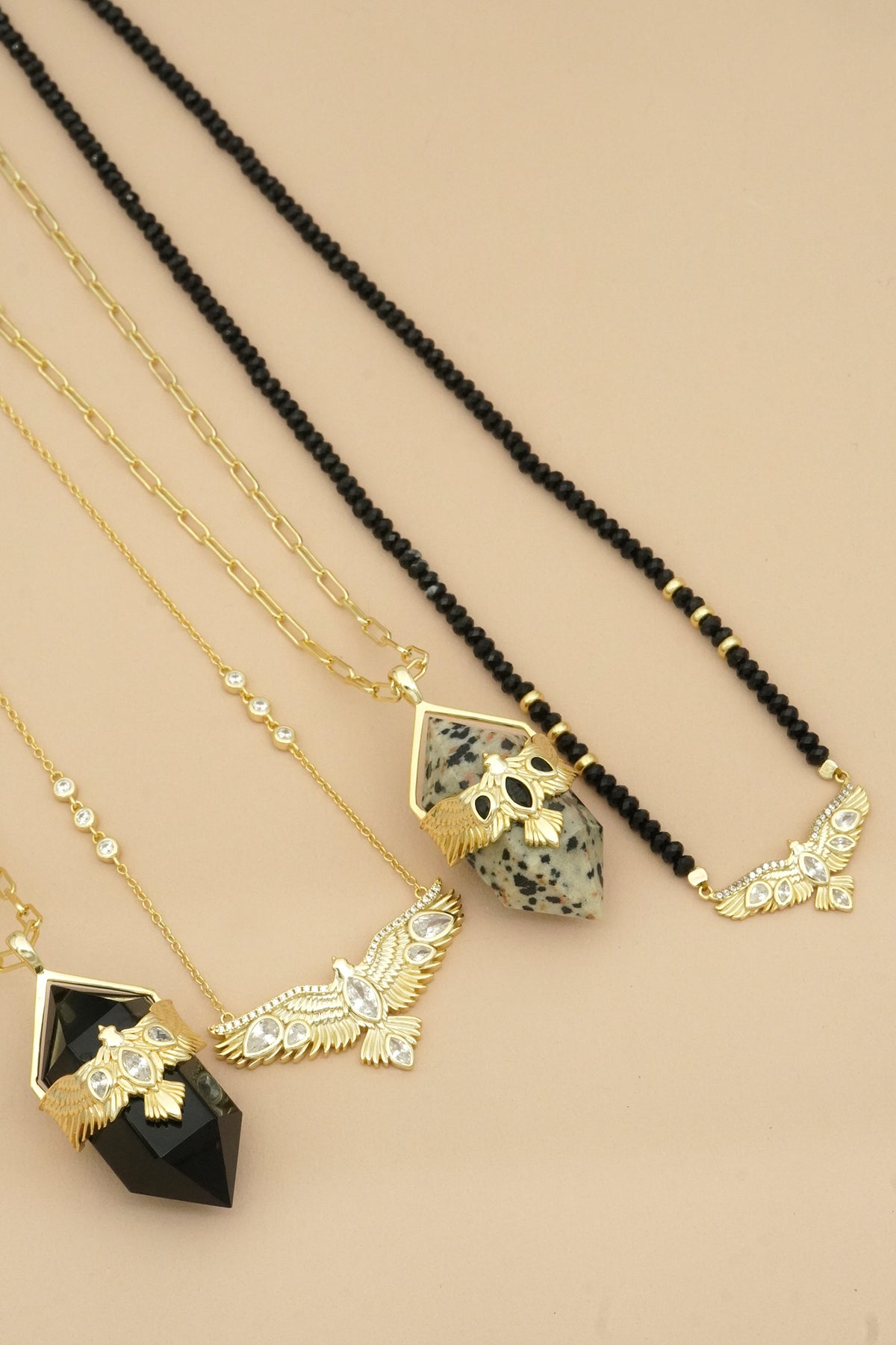 Four necklaces with black and gold soaring hawk pendants on a beige background