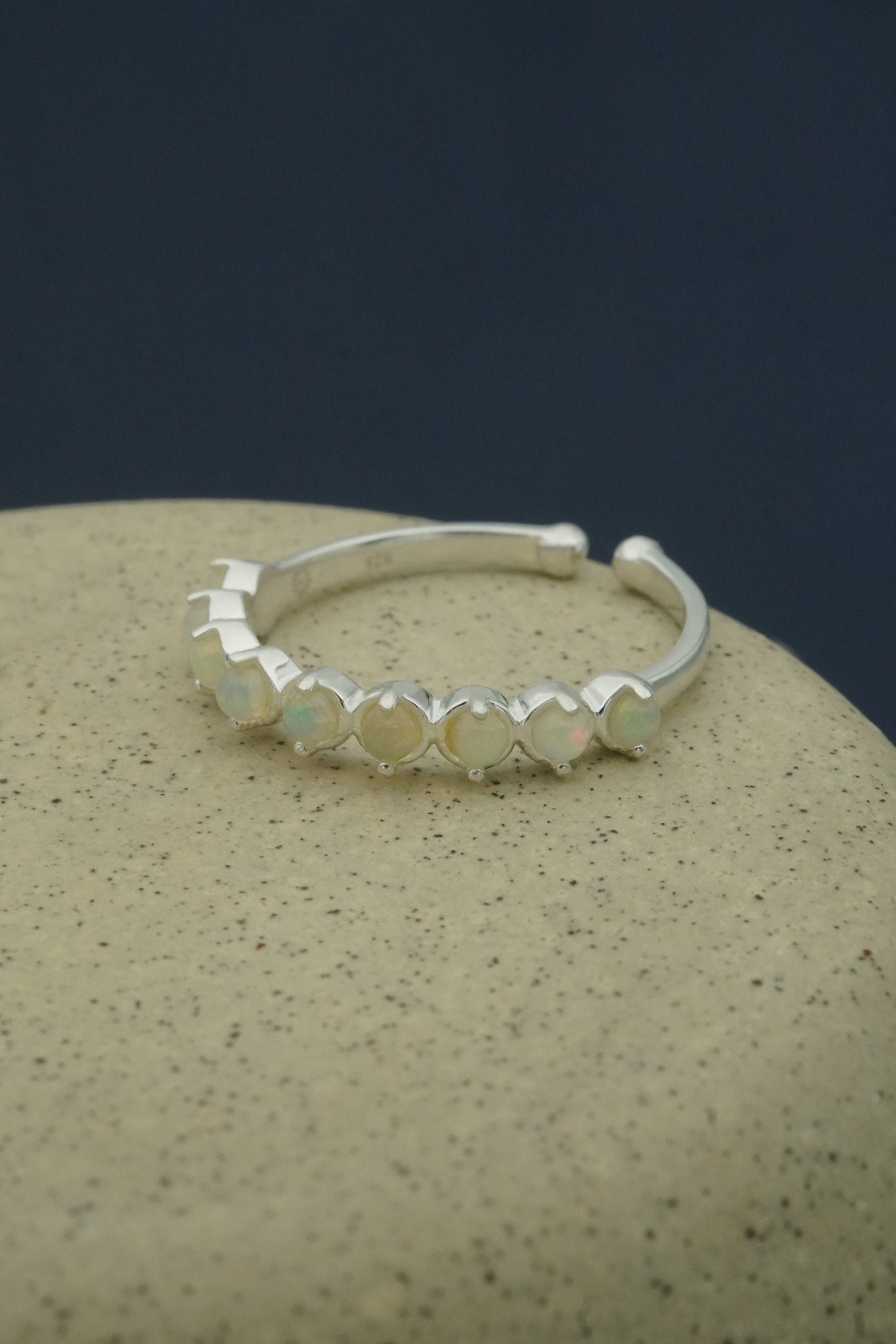 Silver stacking ring with small opal stones on a beige surface